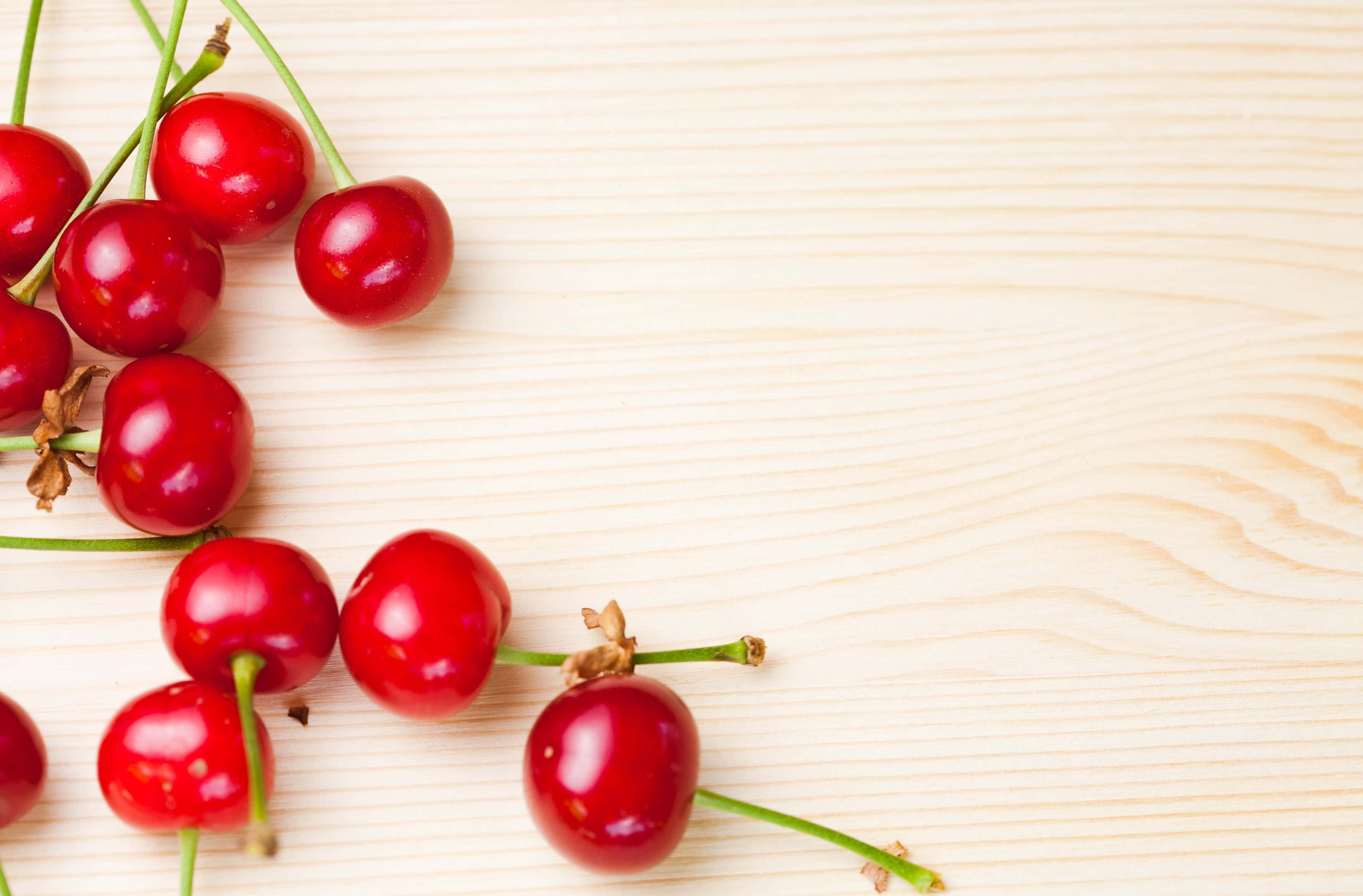 Cherry 桌布 壁紙 — 鮮紅色的櫻桃帶有綠色莖，散落在淺色木質表面上。