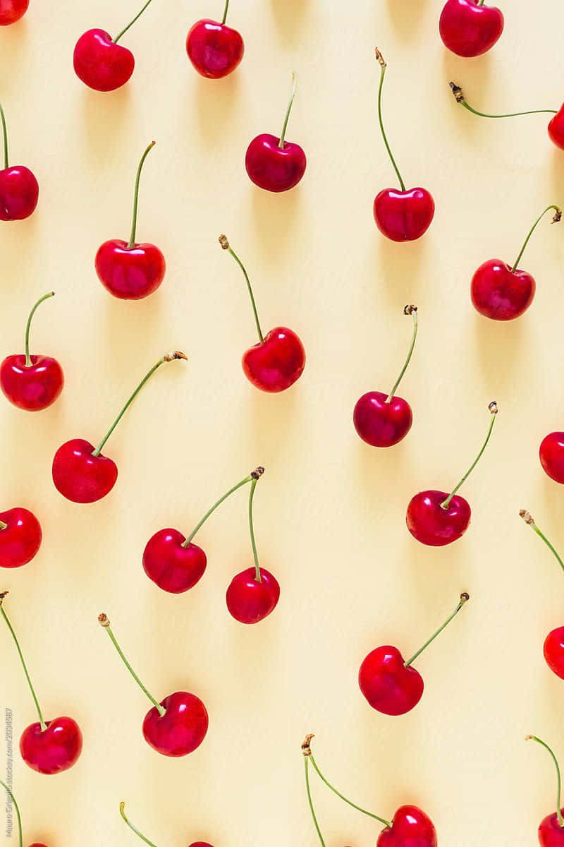Cherry 桌布 壁紙 — 鮮紅色的櫻桃帶有綠色莖部，散落在柔和的黃色背景上，形成平鋪構圖。