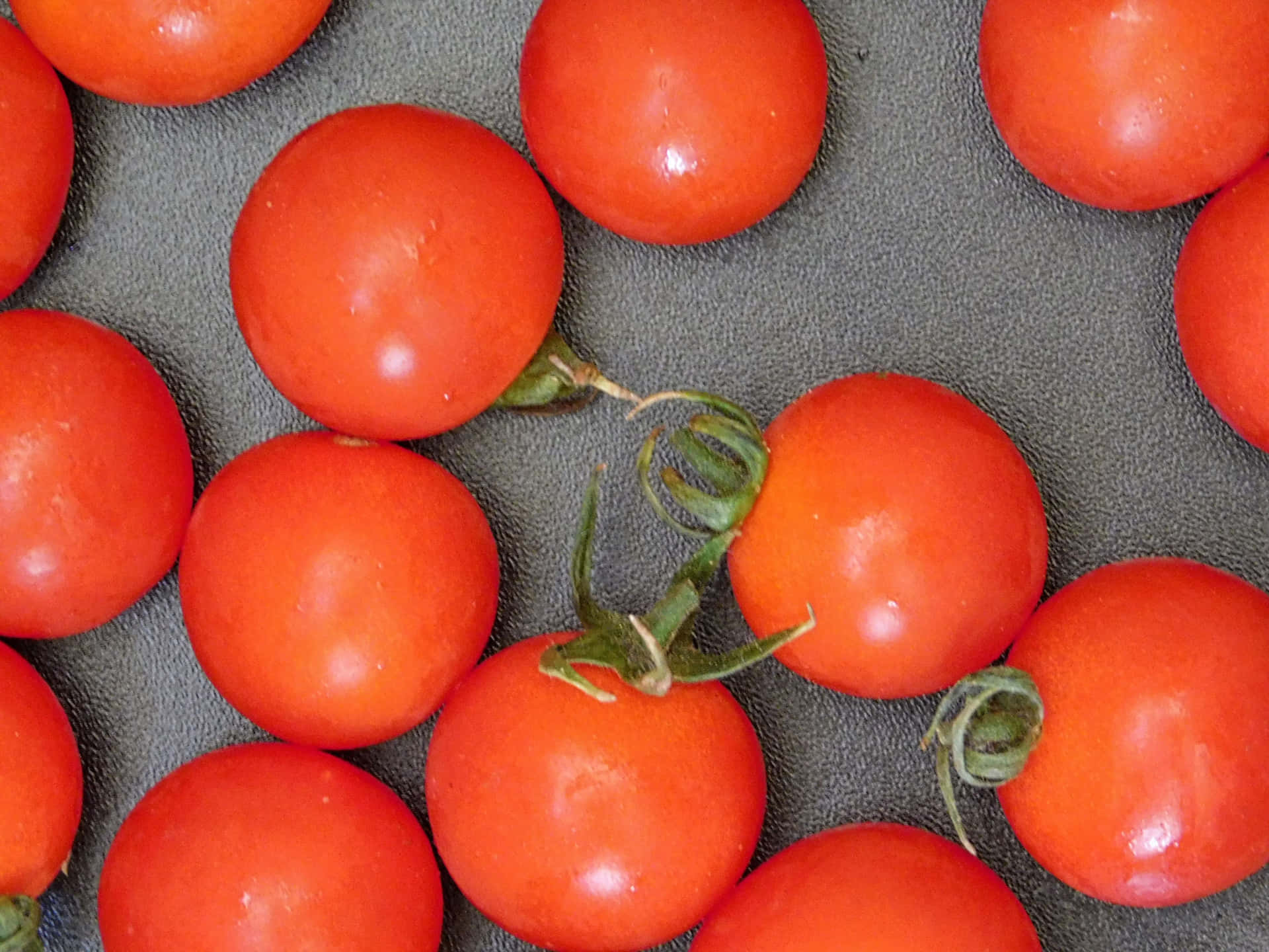 Tomatoes 壁紙 — 鮮紅色的櫻桃番茄搭配綠色莖部，放置在帶有紋理的灰色表面上，以俯拍特寫鏡頭拍攝。
