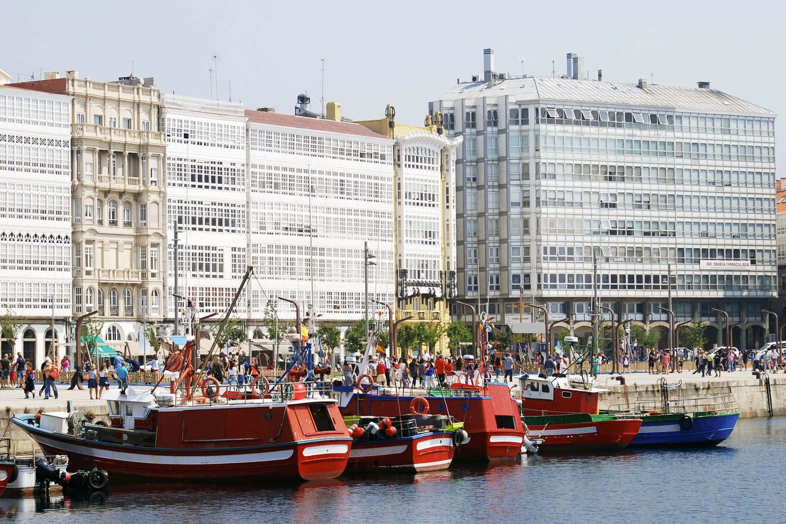 Buildings 桌布 壁紙 — 鮮紅色的漁船停泊在繁忙的港口，歷史與現代建築交錯，天空晴朗。