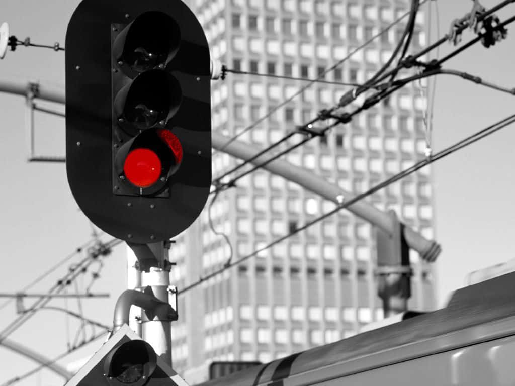 Stop Light 桌布 壁紙 — 鮮紅色的火車信號燈在電線和經過的火車的單色城市背景下發光。