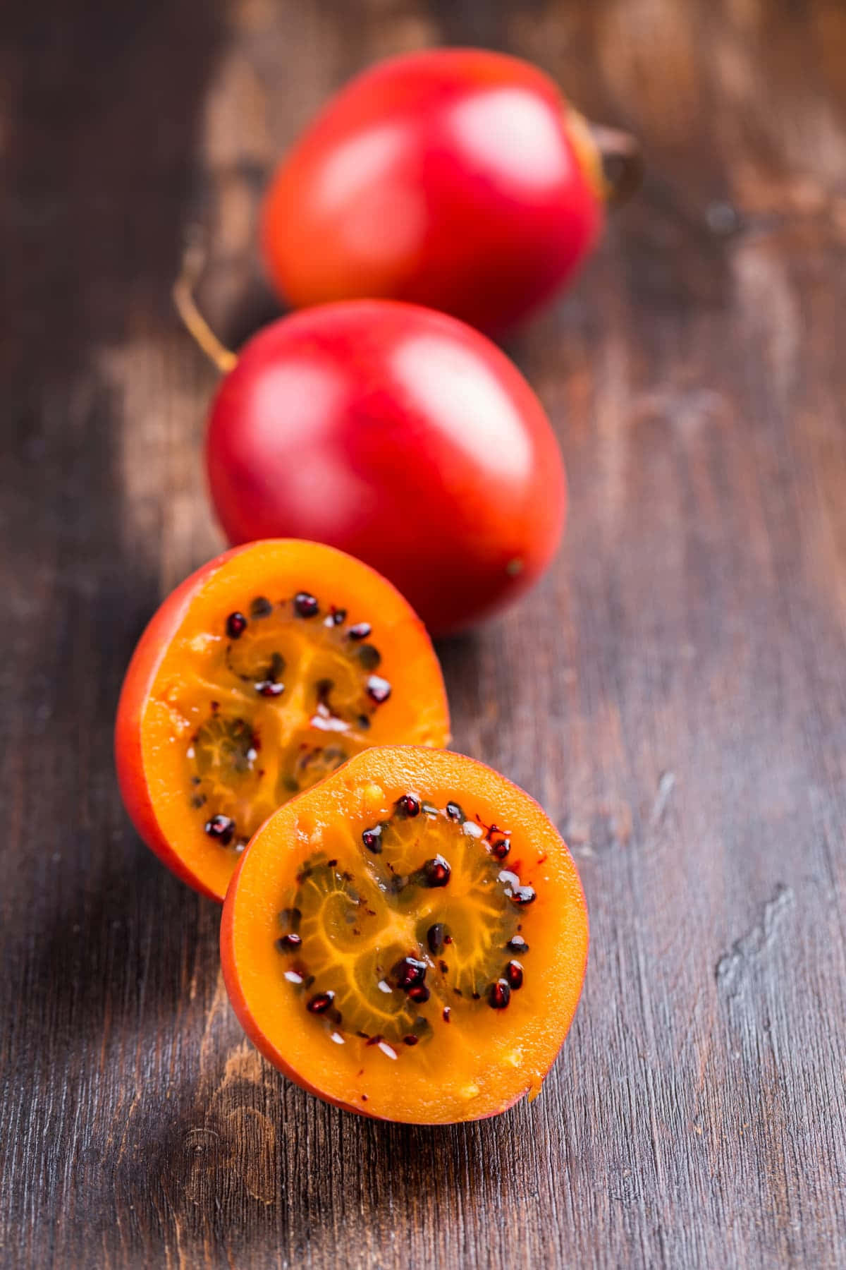 Fruit 桌布 壁紙 — 鮮紅色的百香果，帶有多汁的橙色果肉和黑色種子，放在質樸的深色木質表面上。
