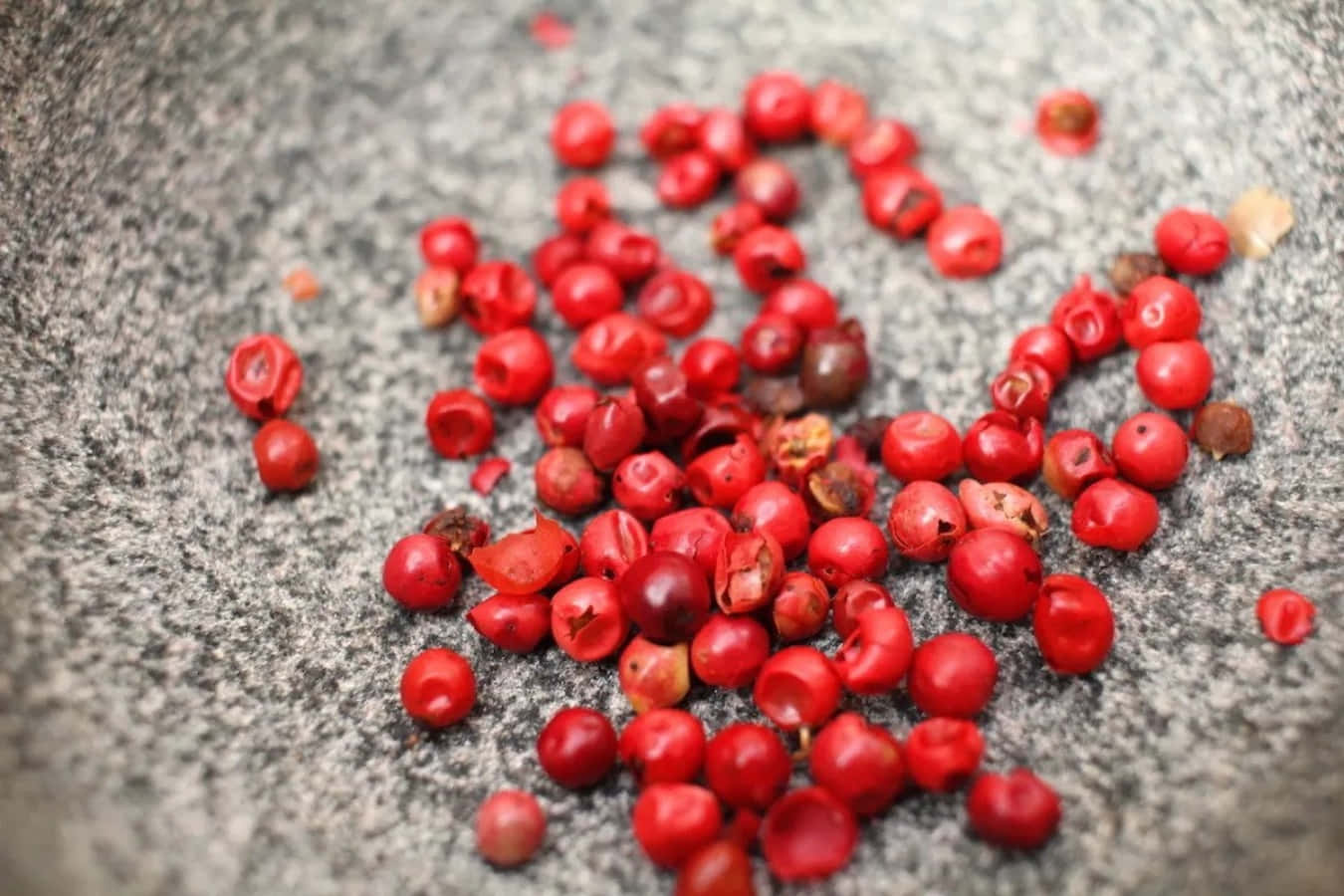 Pink Peppercorn 桌布 壁紙 — 鮮紅色胡椒粒散落在有紋理的灰色石頭表面上，特寫照片。