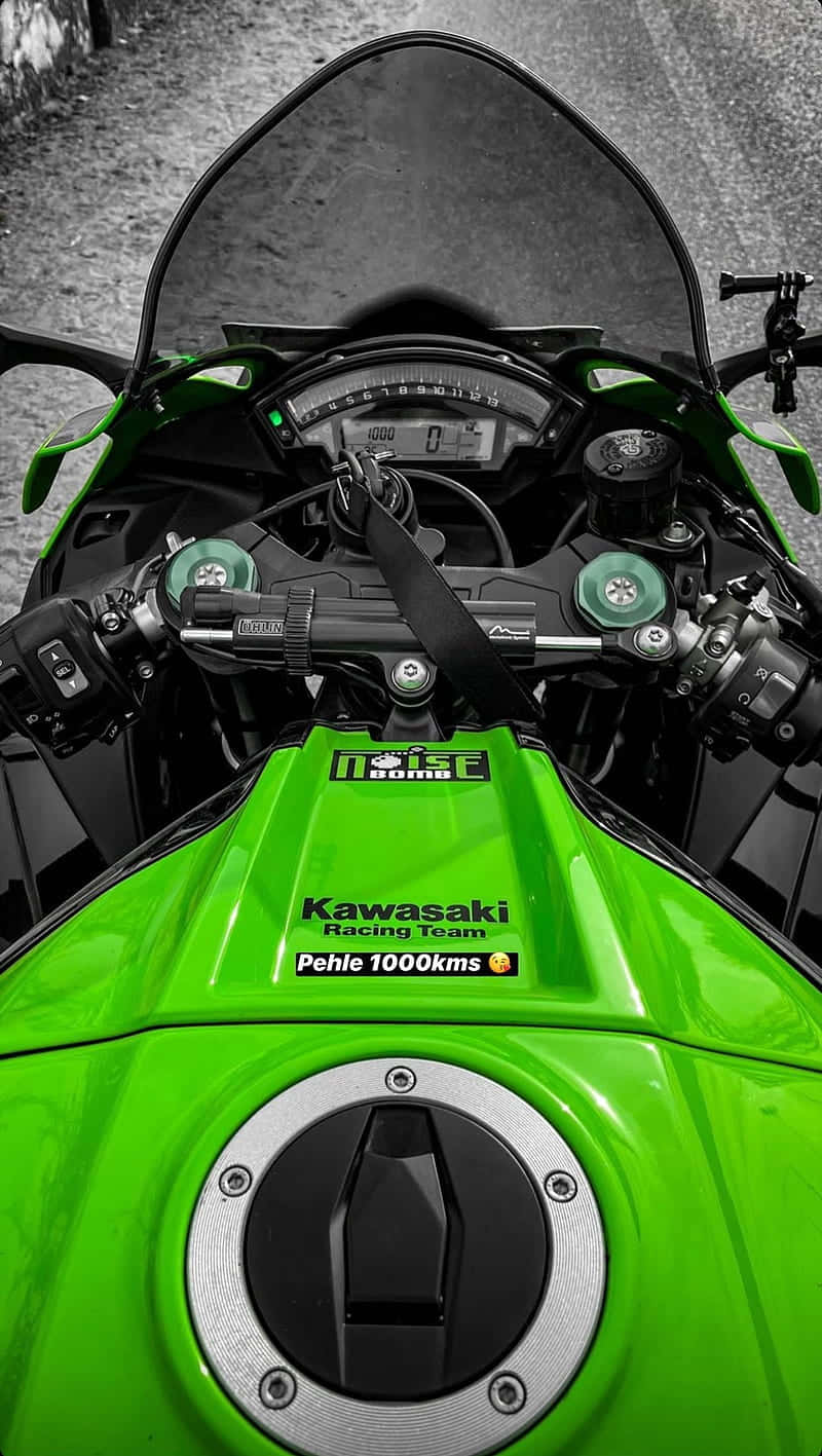 Kawasaki Desktop 桌布 壁紙 — 鮮綠色Kawasaki機車儀表板，帶有'Pehle 1000kms'貼紙，背景為黑白碎石。