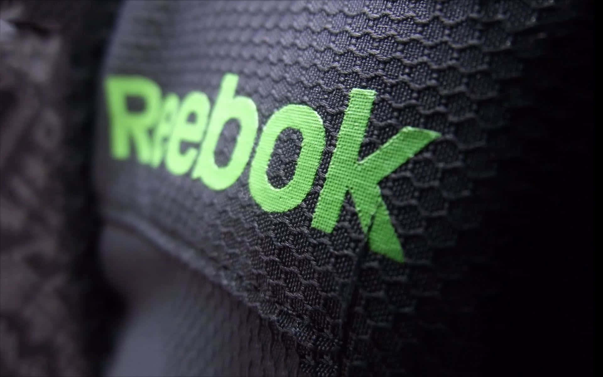 Reebok 桌布 壁紙 — 鮮綠色Reebok標誌近距離特寫，縫在帶有紋理的黑色運動布料上，景深較淺。