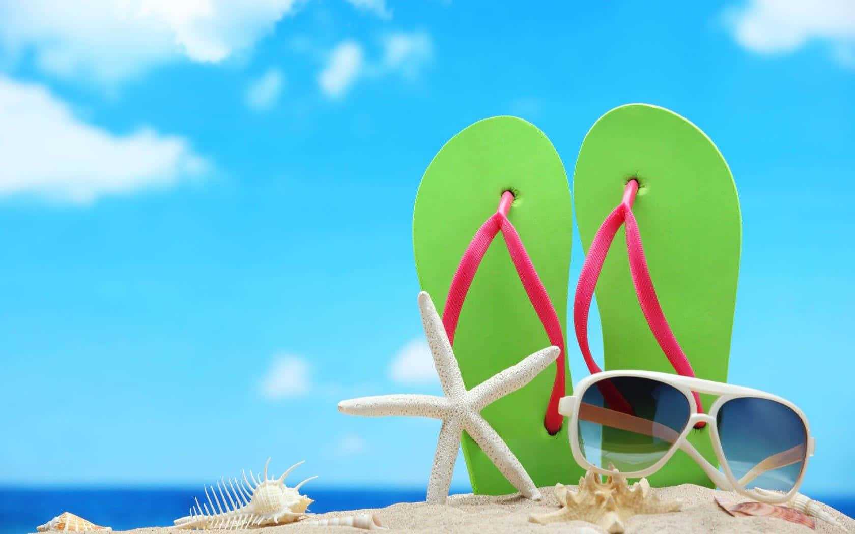 Beach Sandals 桌布 壁紙 — 鮮綠色人字拖搭配粉紅色帶子和白色太陽眼鏡，放置在沙灘上，旁邊有海星和貝殼，天空清澈湛藍。