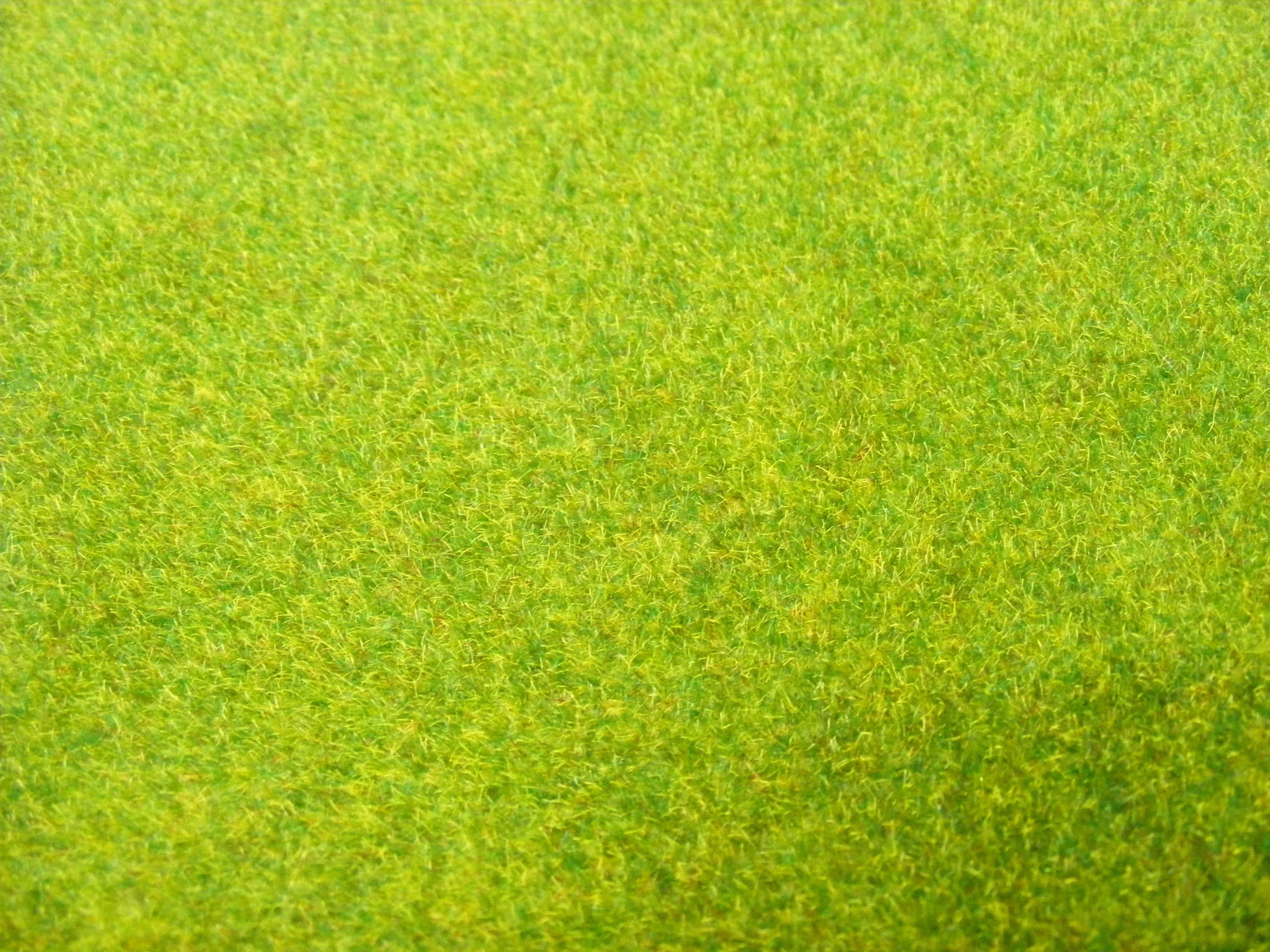 Grass Texture 桌布 壁紙 — 鮮綠色人造草的近距離特寫，帶有淡黃色亮點和紋理纖維，在明亮光線下。