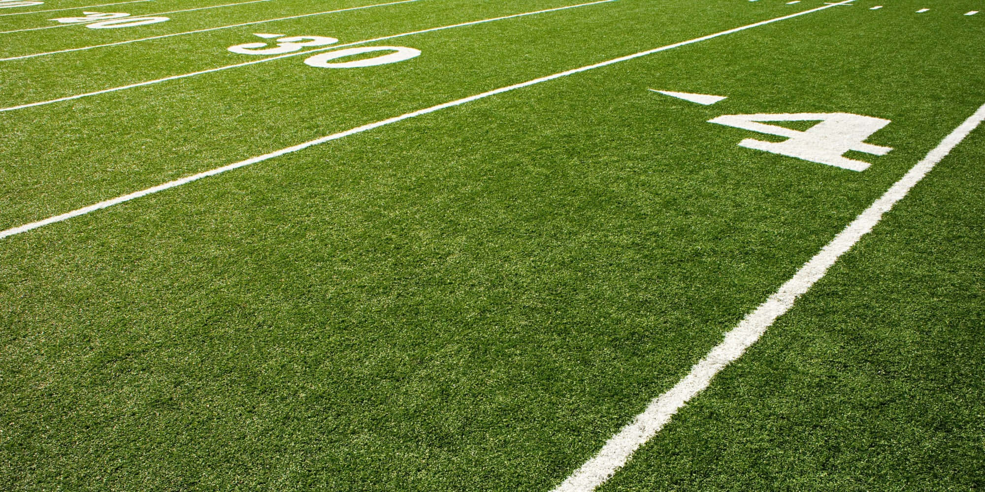 Football Field 桌布 壁紙 — 鮮綠色人造草足球場的特寫，在明亮的日光下帶有清晰的白線和數字。