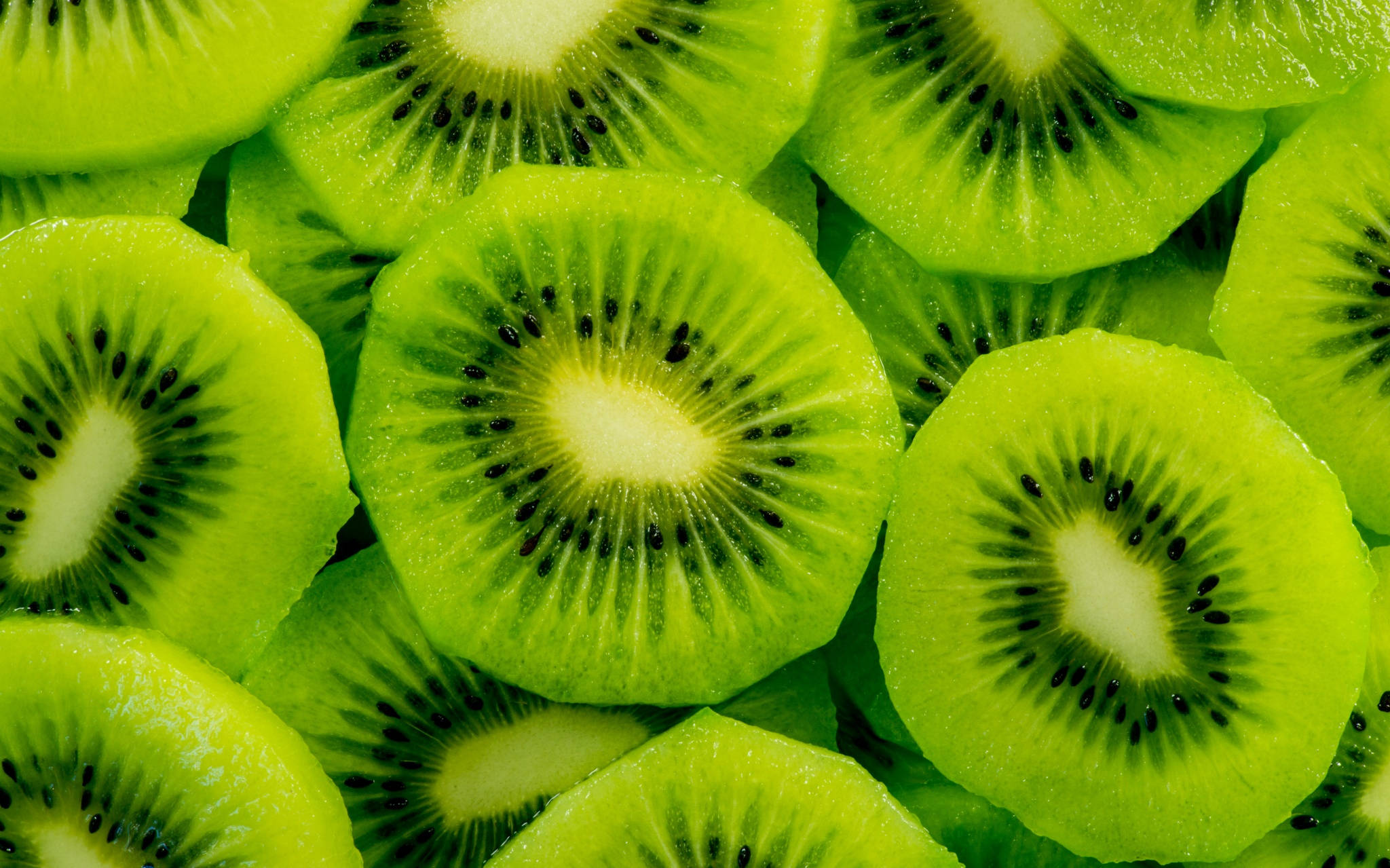 Fruits 桌布 壁紙 — 鮮綠色奇異果切片以密集重疊圖案排列，展示其多汁質地和黑色種子。