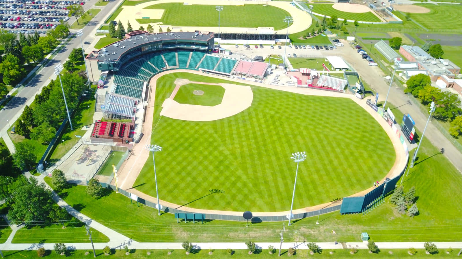 Baseball Field 桌布 壁紙 — 鮮綠色棒球場的鳥瞰圖，整齊條紋的草地和色彩繽紛的座位在明亮的日光下。