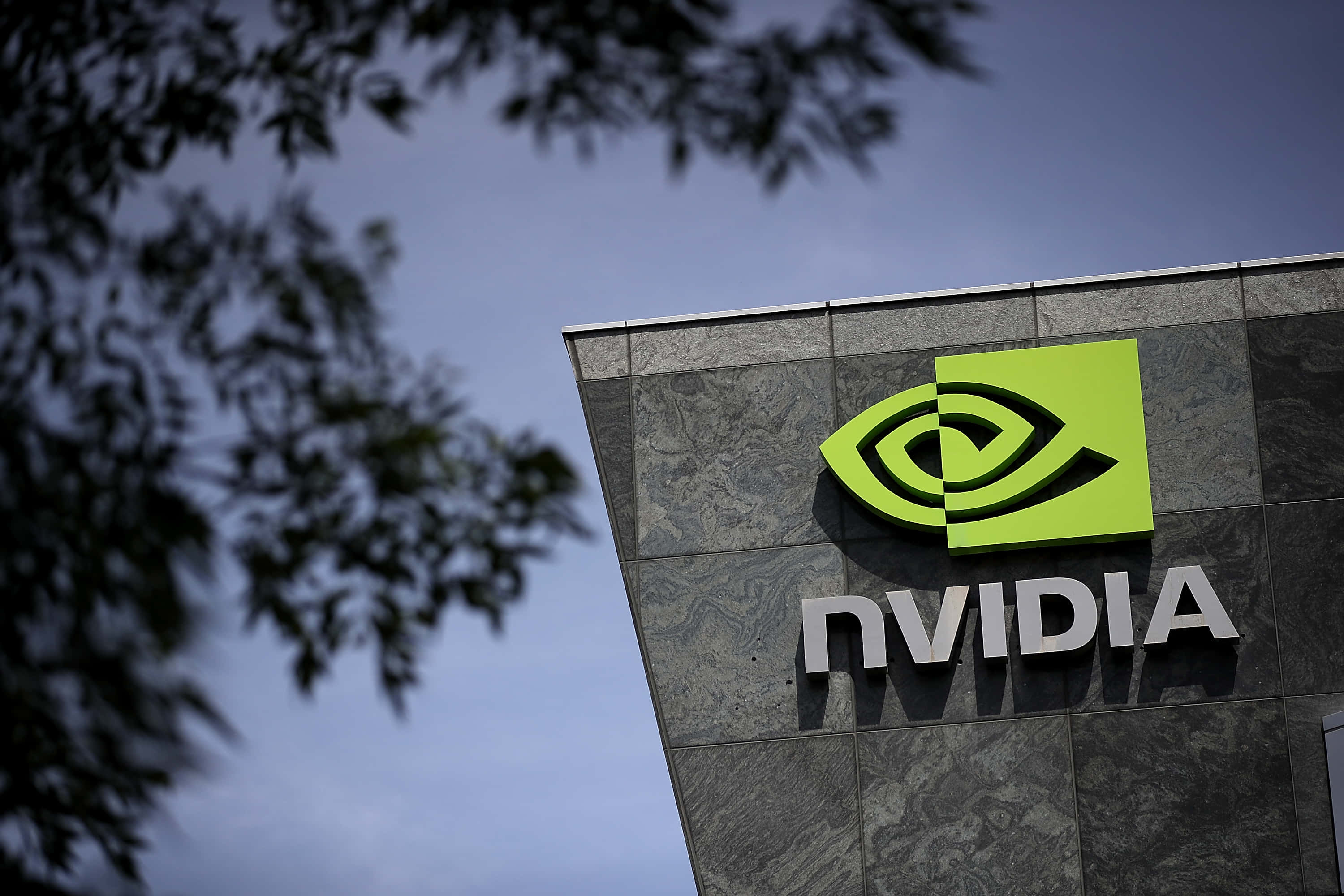 nvidia 桌布 壁紙 — 鮮綠色的NVIDIA標誌在灰色石建築上突出，背景是黃昏天空和剪影樹枝。