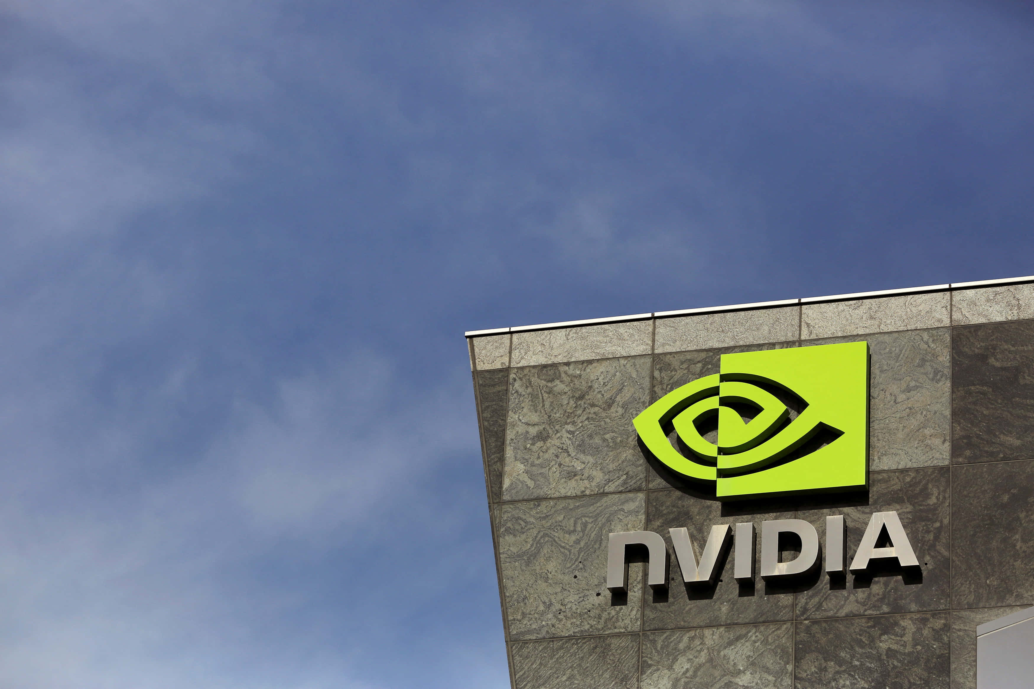 nvidia 桌布 壁紙 — 鮮綠色的NVIDIA標誌在部分多雲的藍天下石建築上突出顯示。