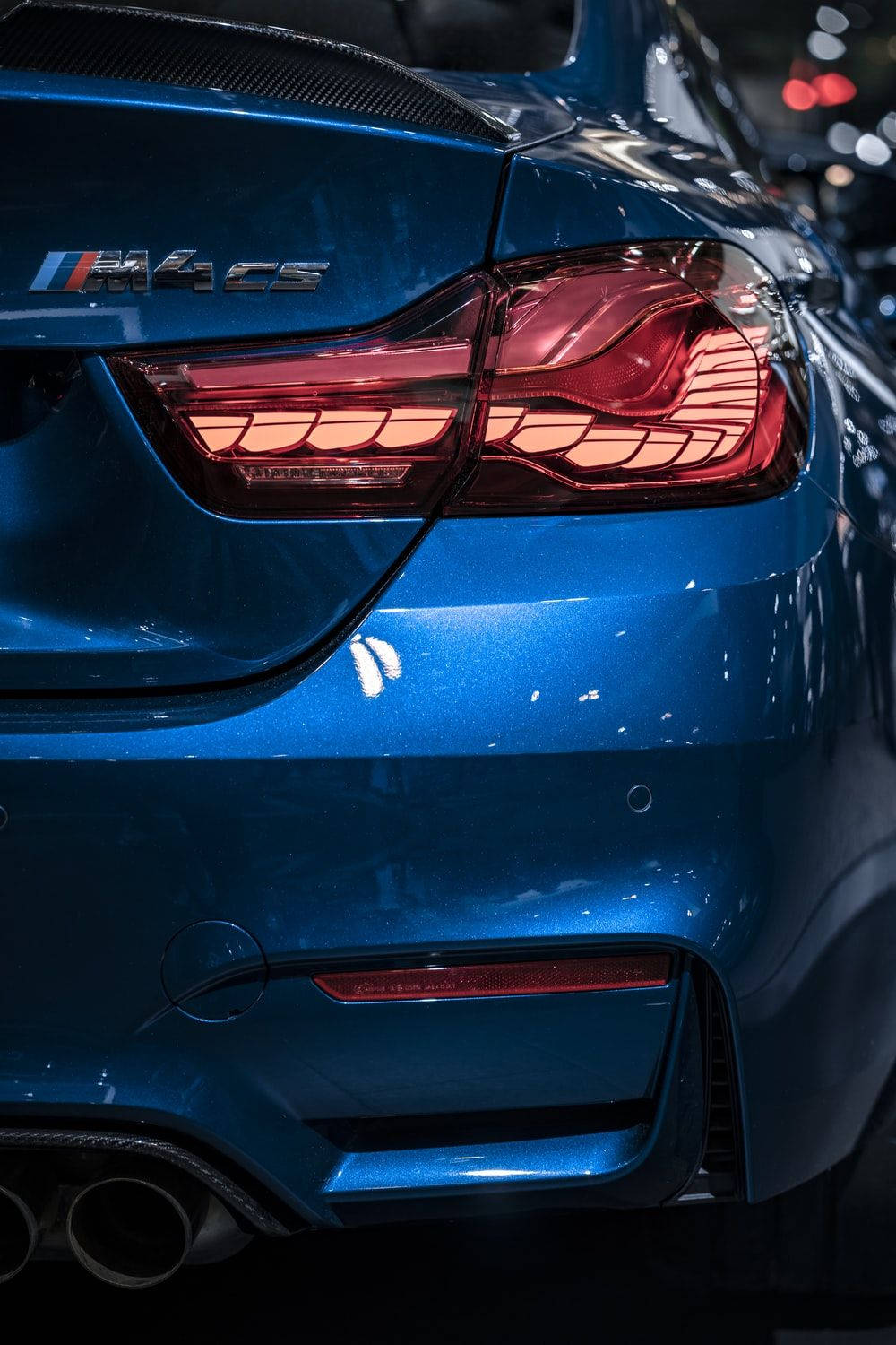 iPhone 桌布 壁紙 — 鮮藍色BMW M4 CS跑車的特寫，在環境燈光下展示其時尚的尾燈和碳纖維細節。