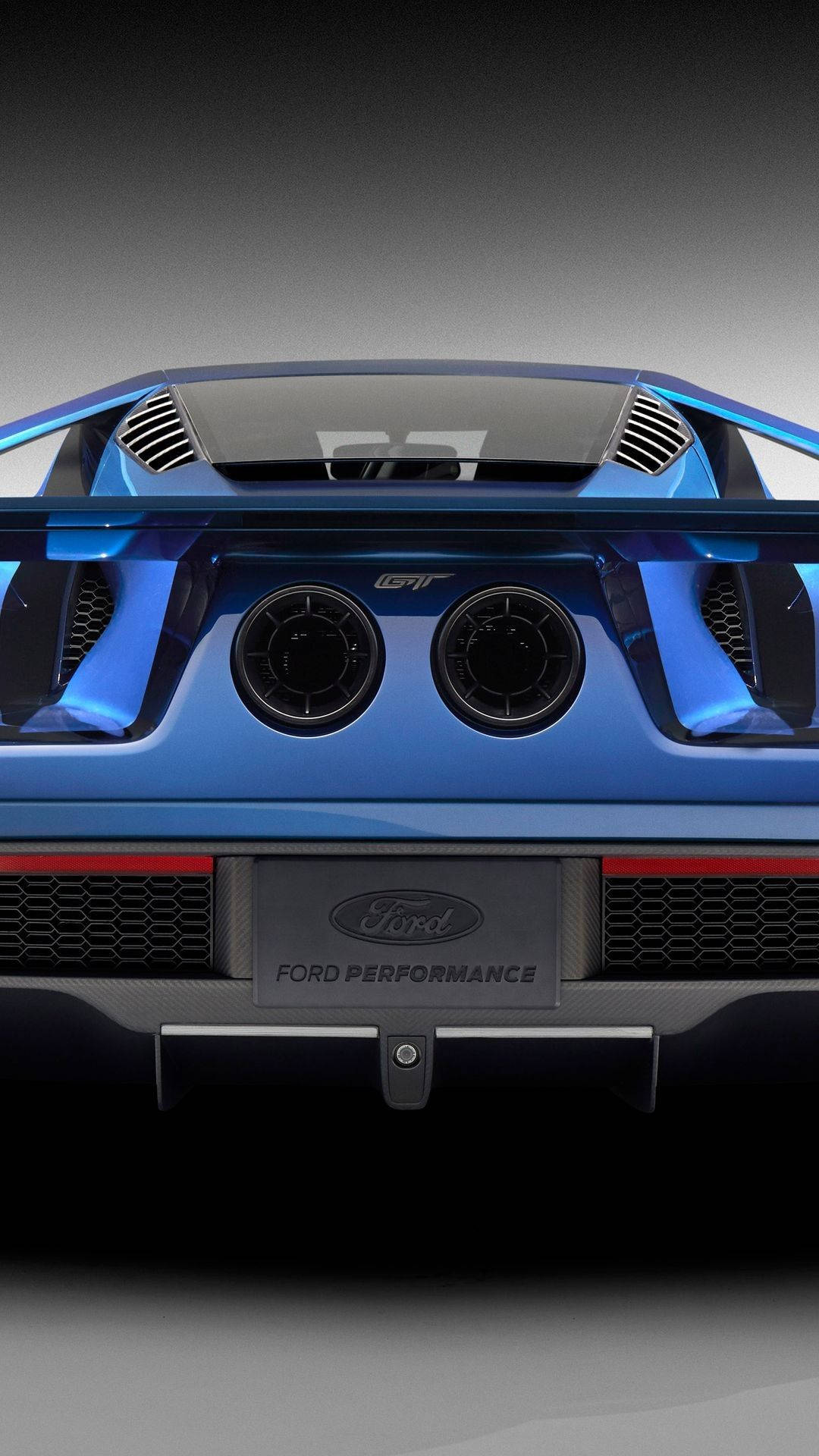 ford iPhone 桌布 壁紙 — 鮮藍色福特GT的緊湊後視圖，配備雙排氣管和碳纖維飾邊，背景為漸變灰色。