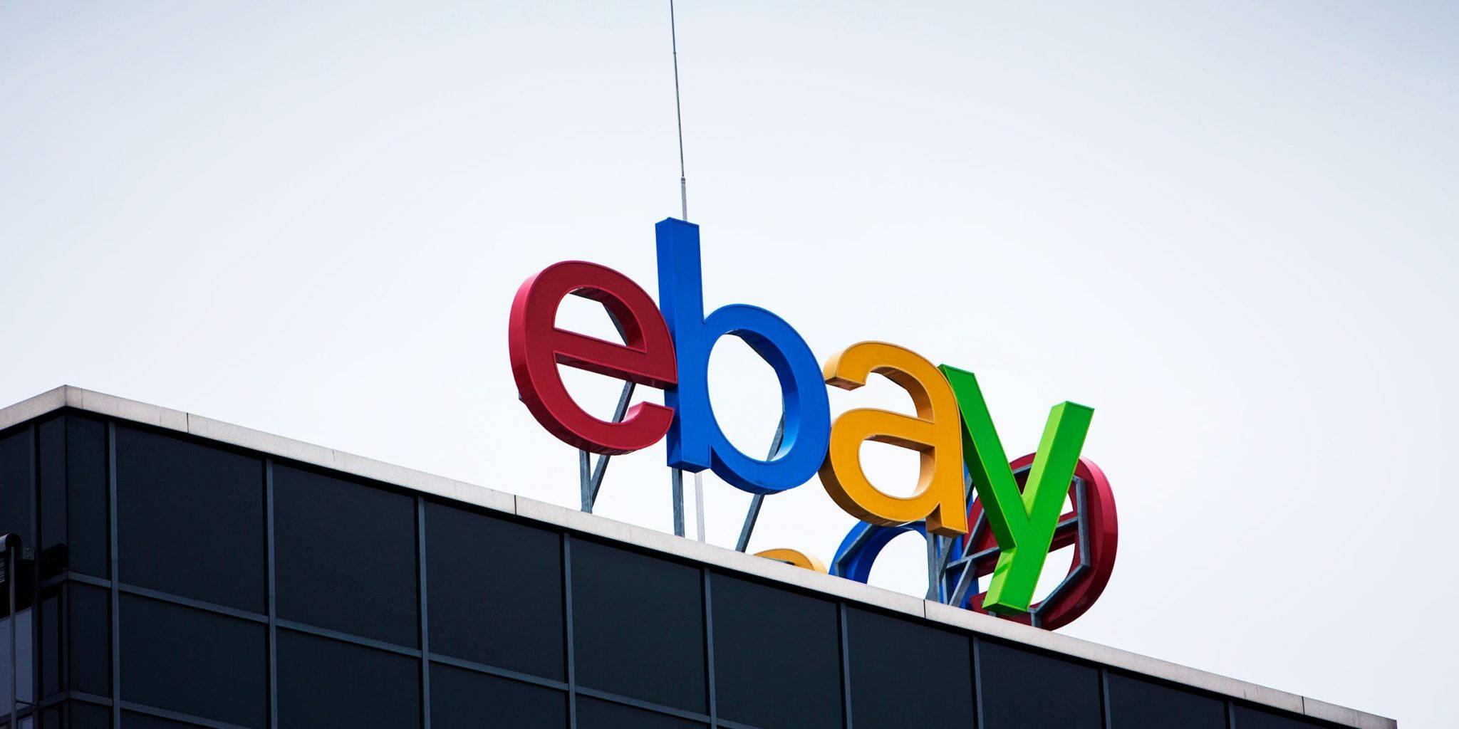 eBay 桌布 壁紙 — 鮮豔多彩的eBay標誌字母安裝在現代玻璃建築頂部，襯著淡色天空。