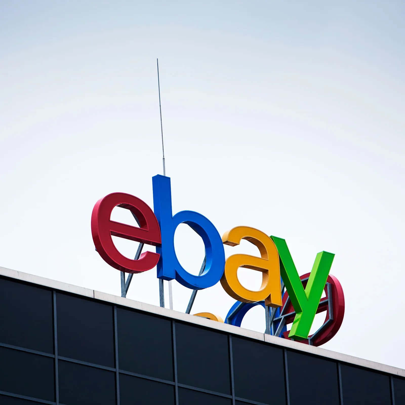 eBay 桌布 壁紙 — 鮮豔多彩的eBay標誌字母安裝在現代玻璃建築頂部，映襯著淡色天空。
