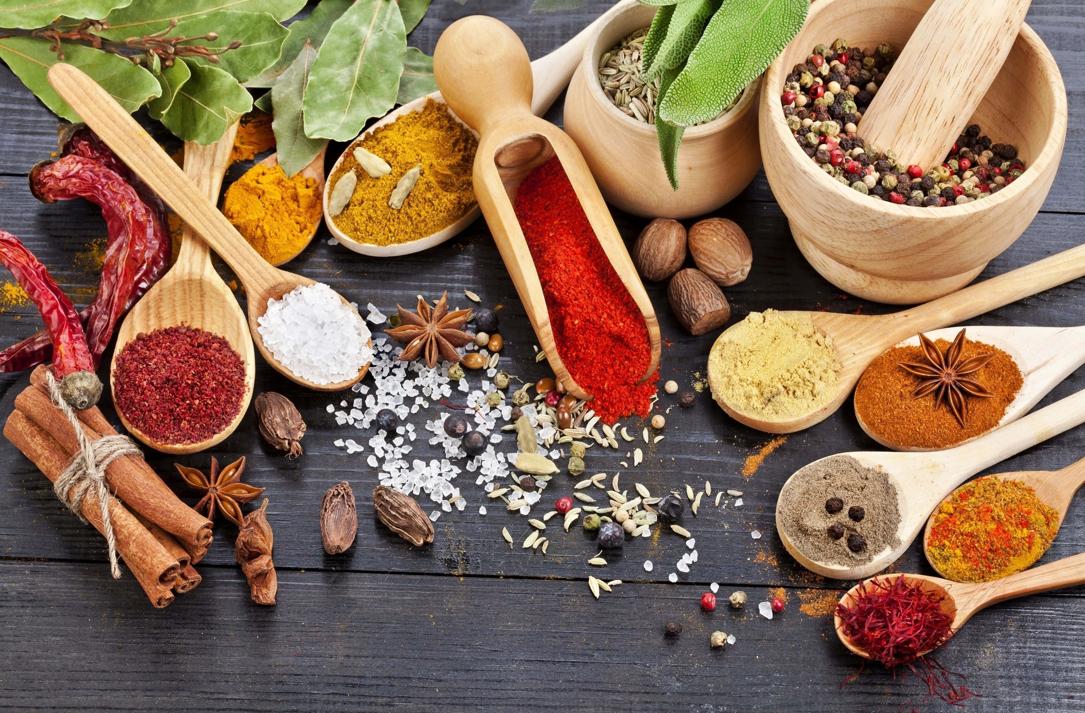 Spice 桌布 壁紙 — 鮮豔多彩的香料和香草，放在木勺和碗中，散落在深色質樸的木質表面上。