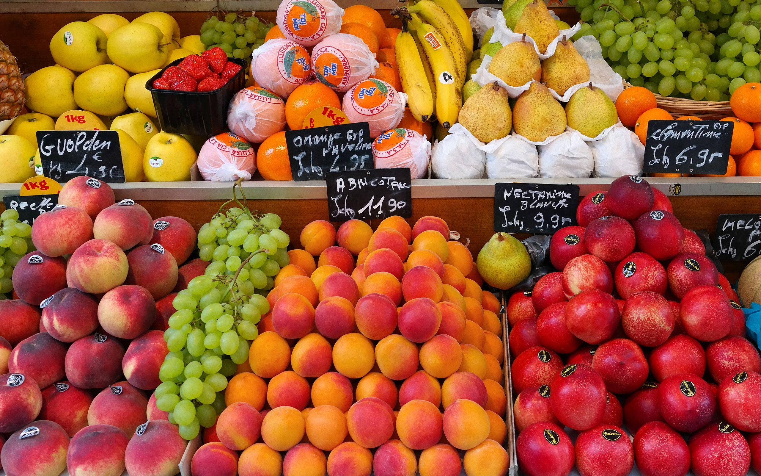 Fruits 桌布 壁紙 — 鮮豔展示新鮮水果，如蘋果、桃子、葡萄和柳橙，在繁忙的市場攤位上排列成色彩繽紛的堆疊。