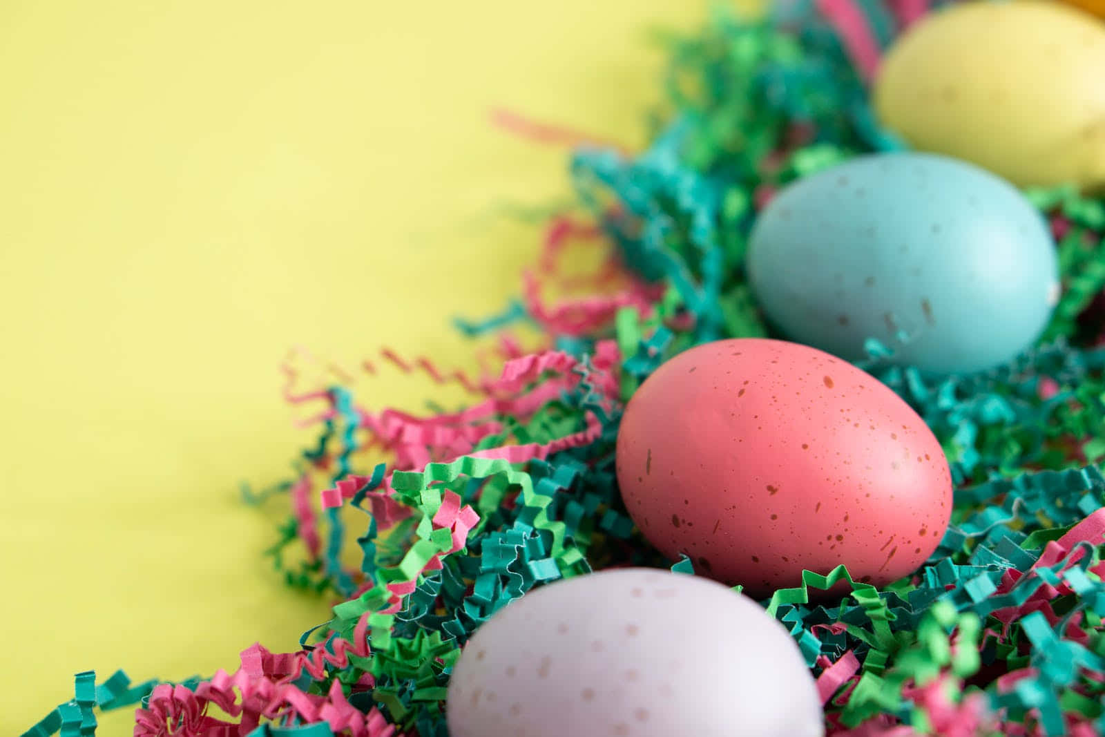 Pastel Easter 桌布 壁紙 — 鮮豔斑點復活節蛋依偎在彩色碎紙中，背景為亮黃色。