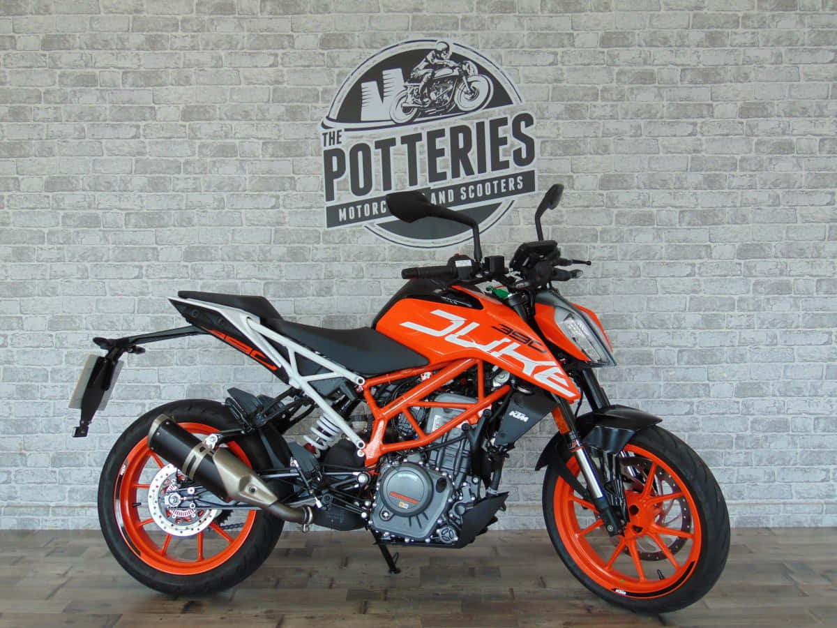 機車 桌布 壁紙 — 鮮豔橙色KTM Duke機車停放在室內，背景是帶有經銷商標誌的灰色磚牆。