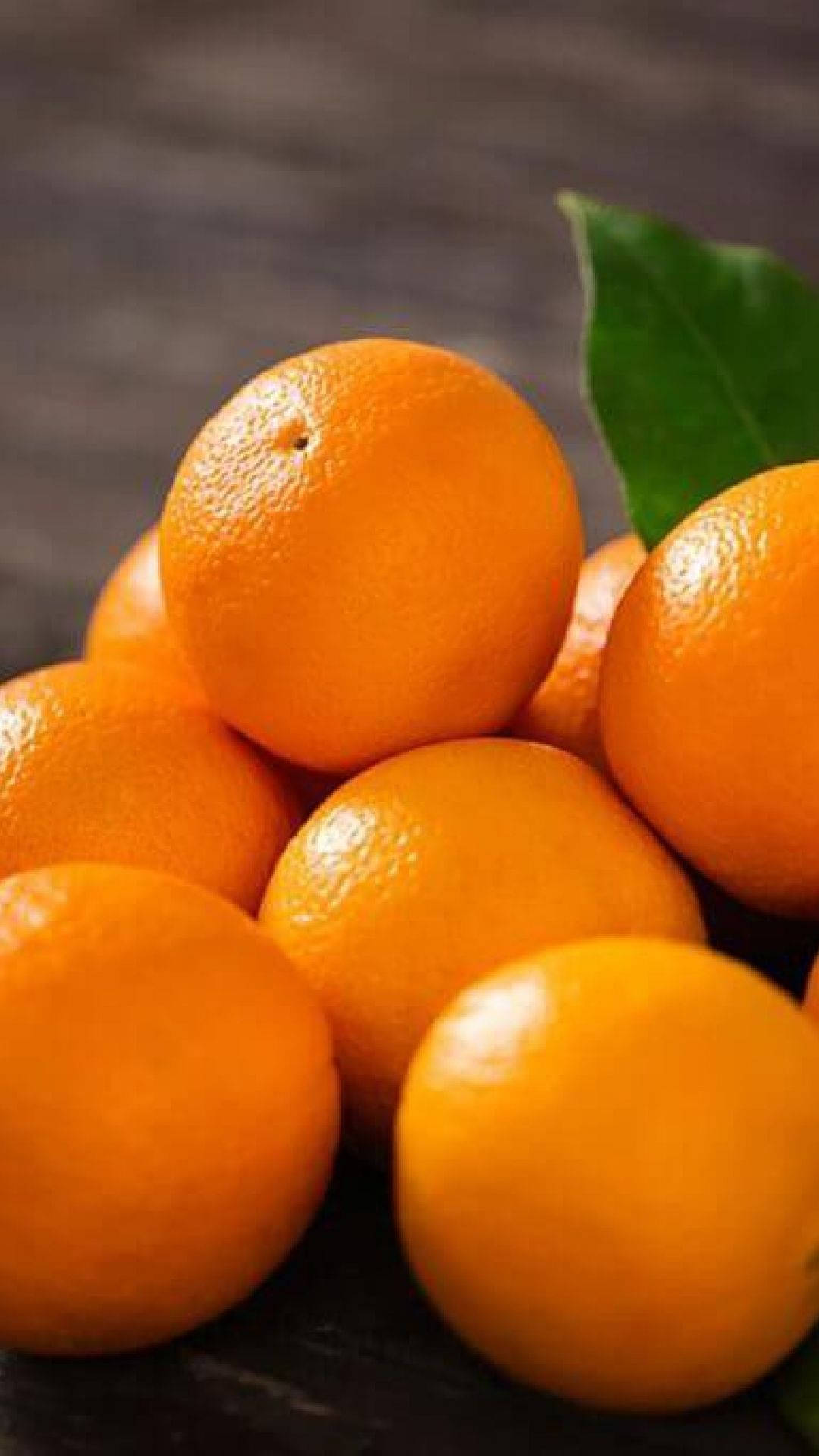 Fruit 桌布 壁紙 — 鮮豔橙色水果的特寫，一片綠葉放在深色木質表面上。