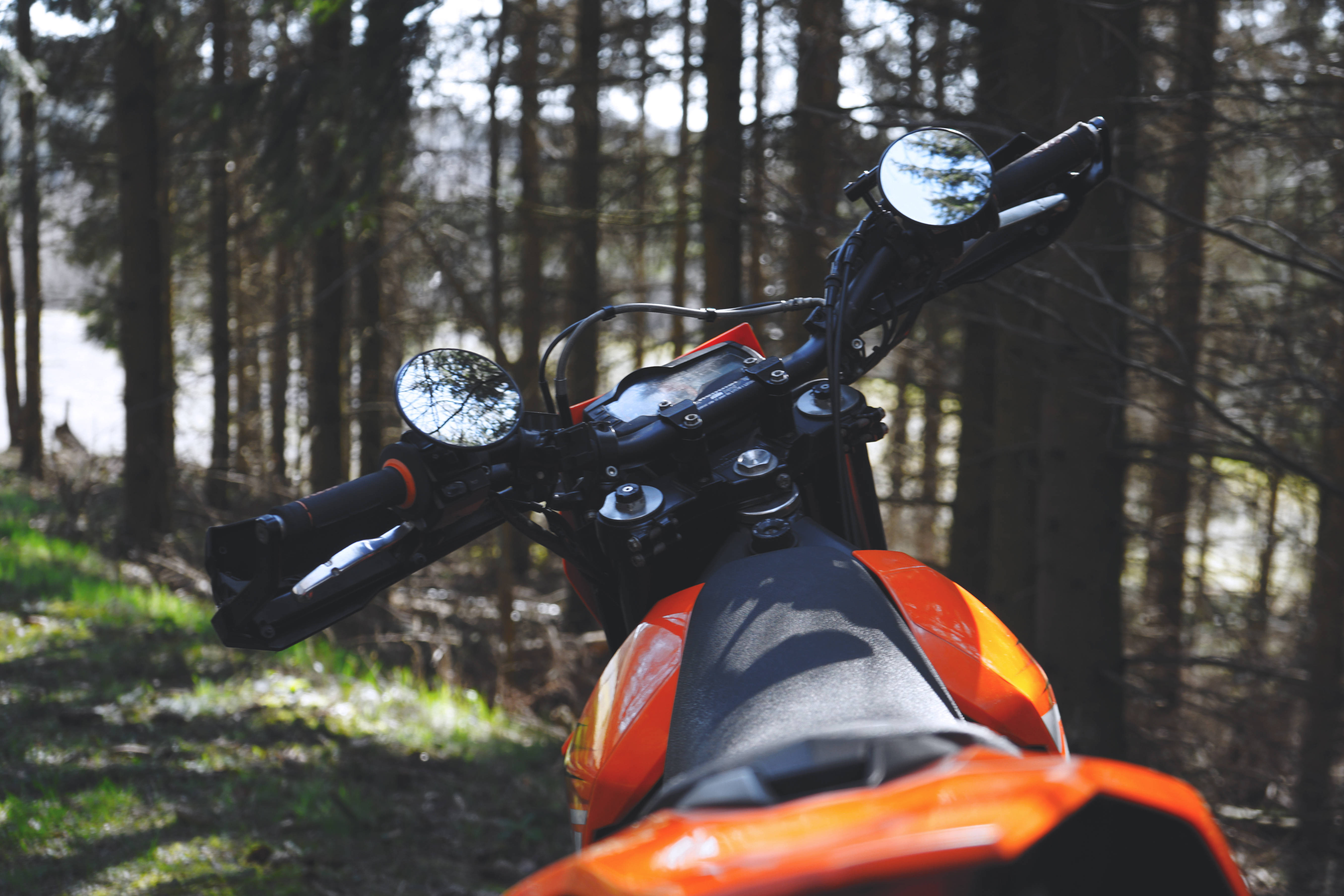 Ktm Bike 桌布 壁紙 — 鮮豔橙色越野機車停放在陽光普照的森林中，有高大的樹木和斑駁的陰影。