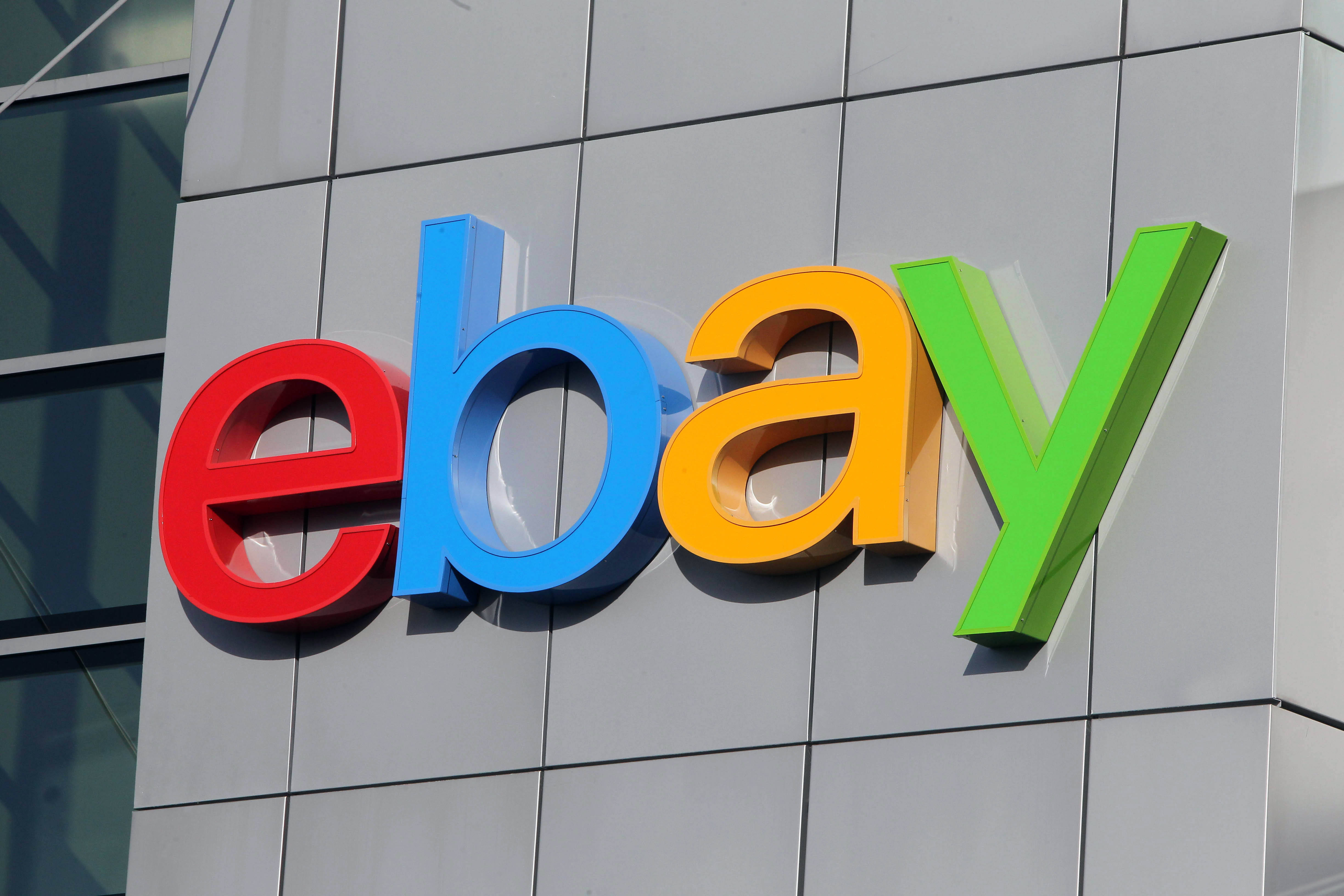 eBay 桌布 壁紙 — 鮮豔的3D eBay標誌，以紅色、藍色、黃色和綠色呈現，安裝在現代灰色瓷磚建築外牆上。