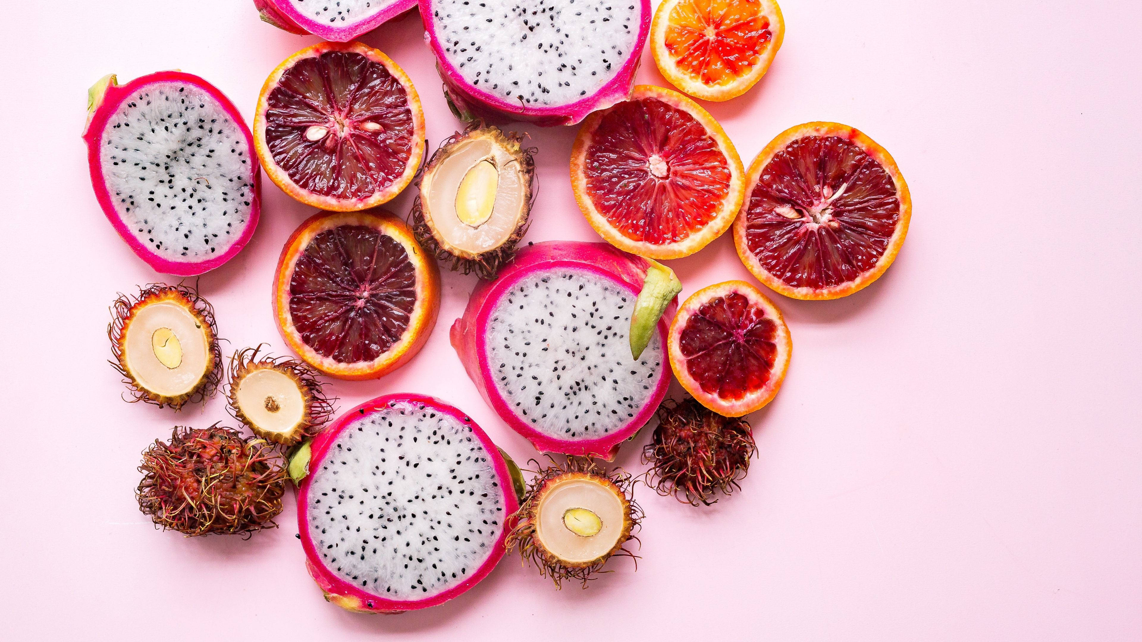 Fruits 桌布 壁紙 — 鮮豔的切片熱帶水果如火龍果和血橙，排列在柔和的粉紅色背景上。