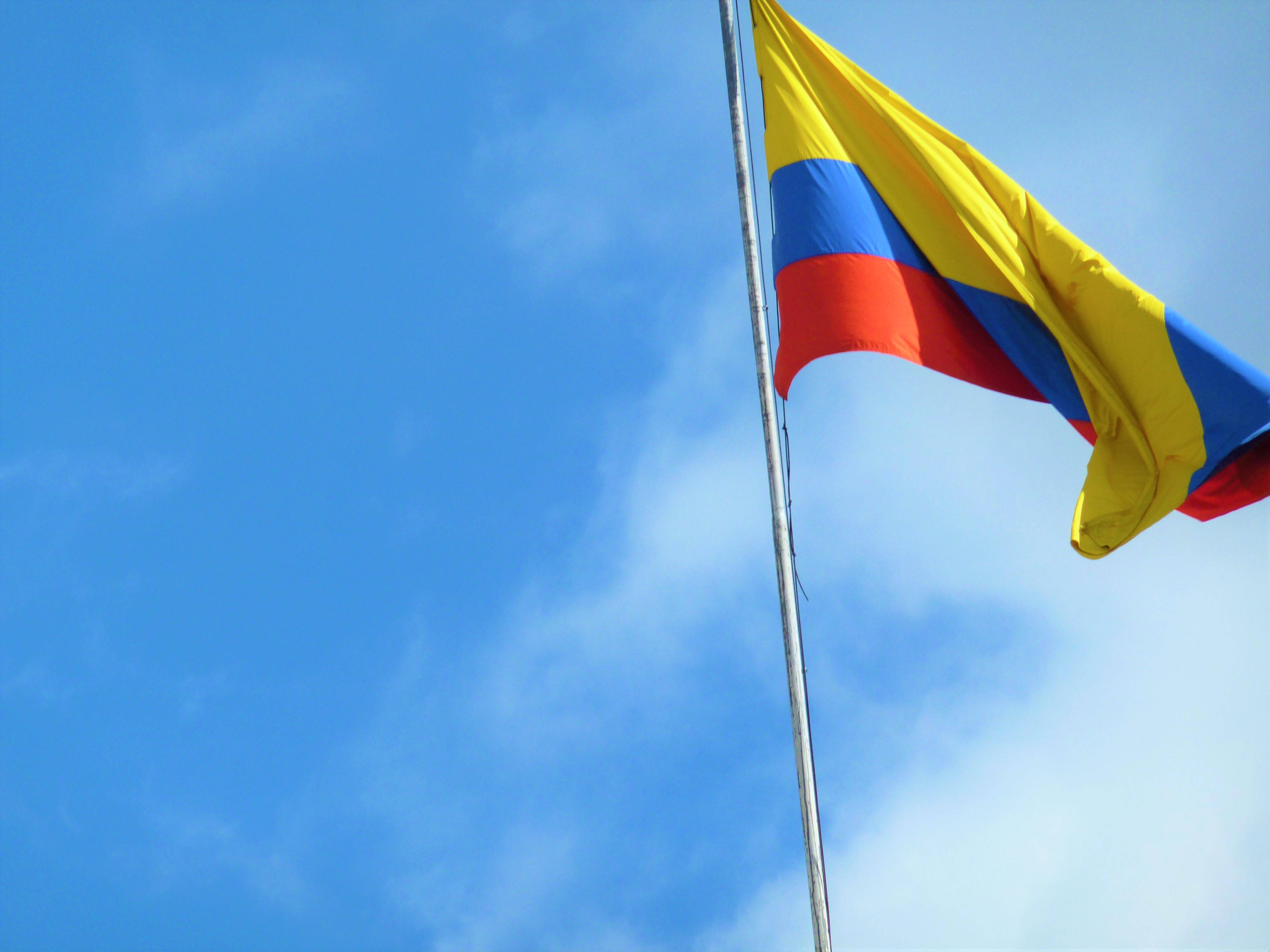 Colombia Flag 桌布 壁紙 — 鮮豔的哥倫比亞國旗，帶有黃色、藍色和紅色條紋，在晴朗的藍天和縷縷白雲中自豪地飄揚。