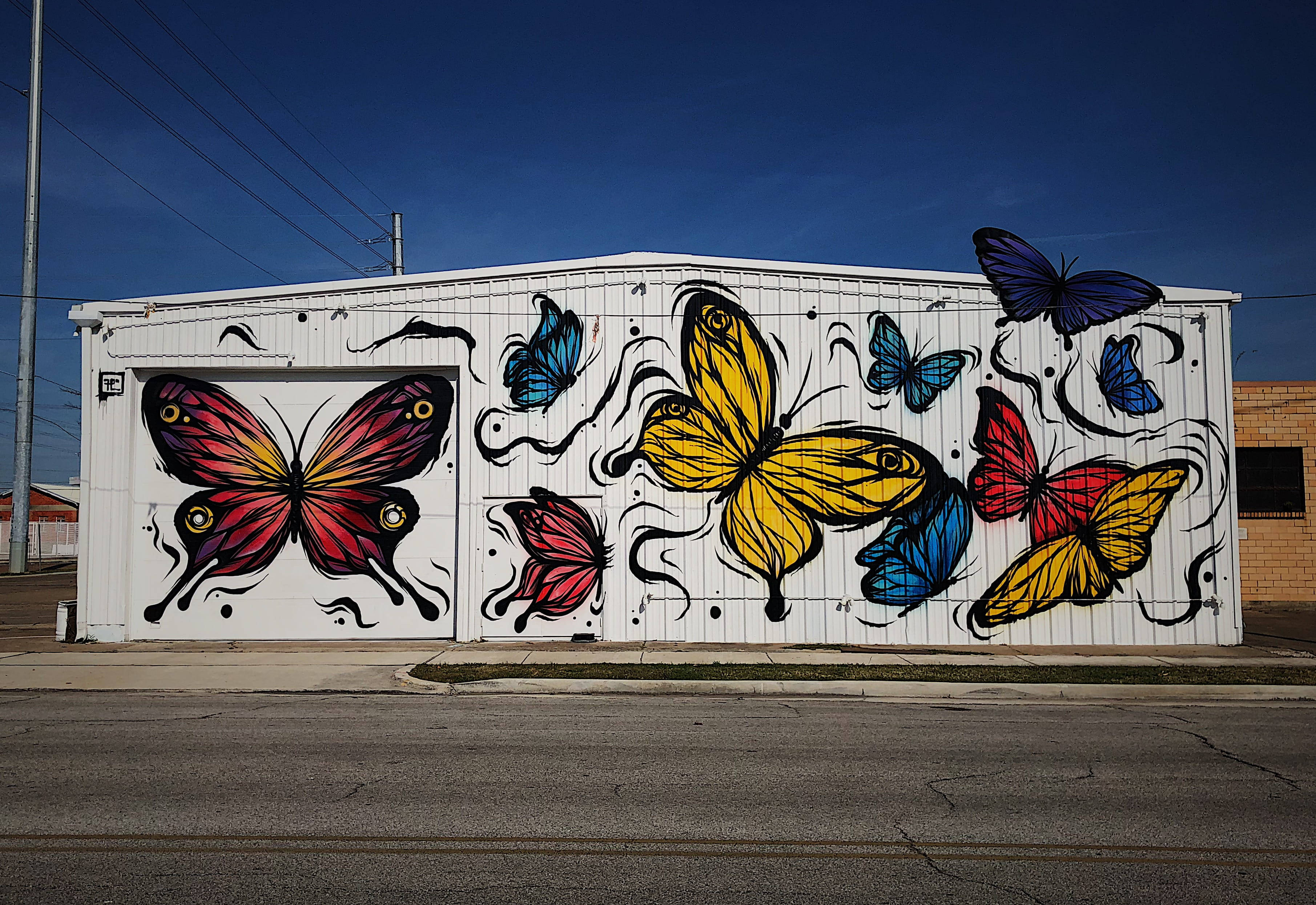 Butterflies 桌布 壁紙 — 鮮豔的塗鴉蝴蝶以紅、黃、藍色在晴朗藍天下飛越白色倉庫牆壁。