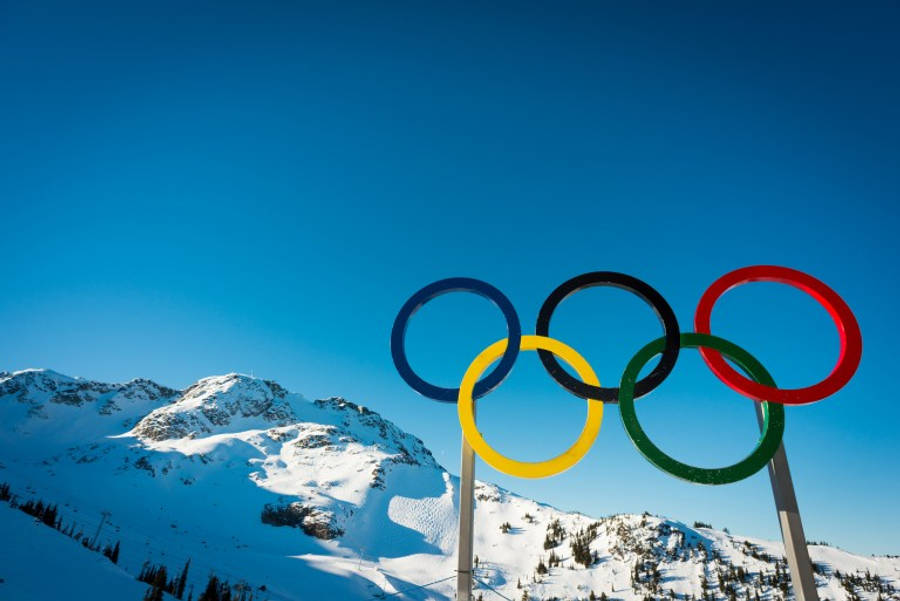 Winter Olympics 桌布 壁紙 — 鮮豔的奧運五環在晴朗的藍天下聳立，背景是白雪覆蓋的山脈。