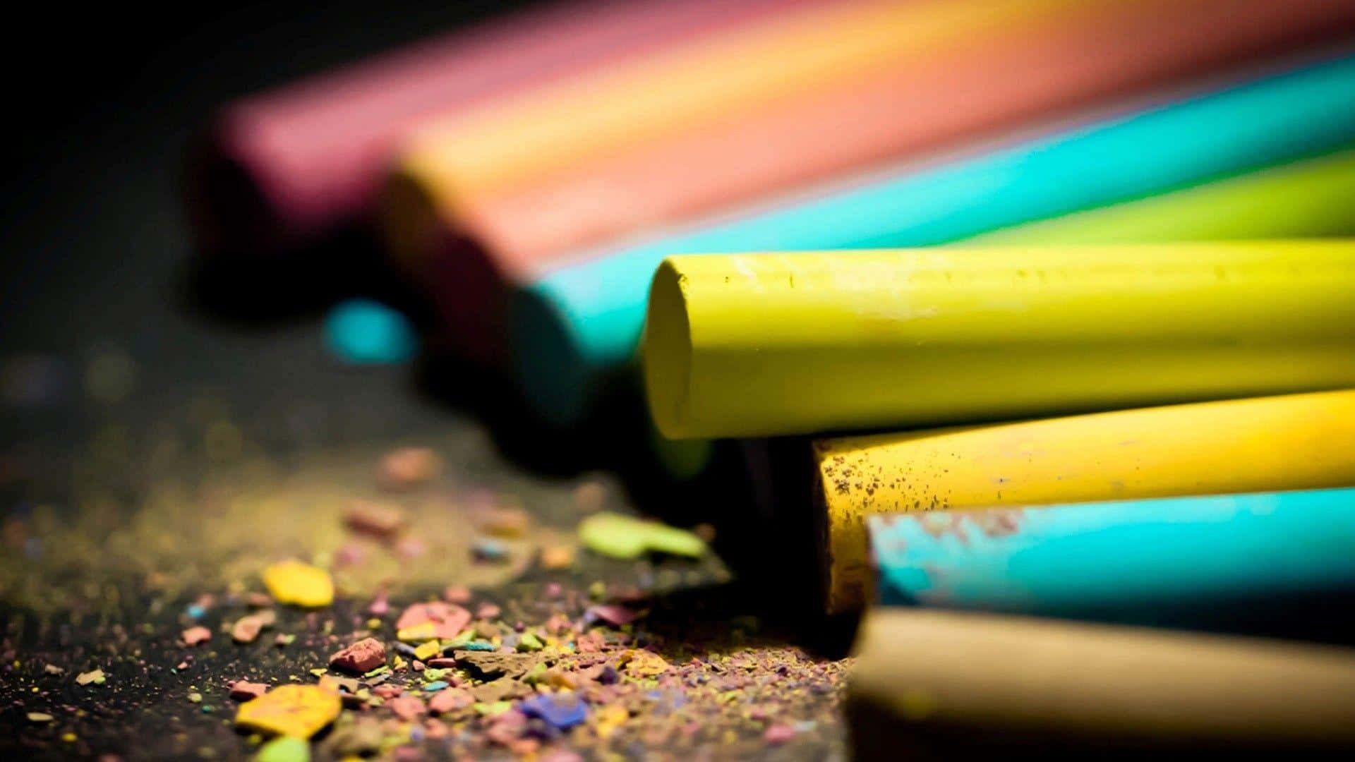 crayon 桌布 壁紙 — 鮮豔的彩色粉筆以對角線放置，在柔和光線下，深色表面上散落著粉末。