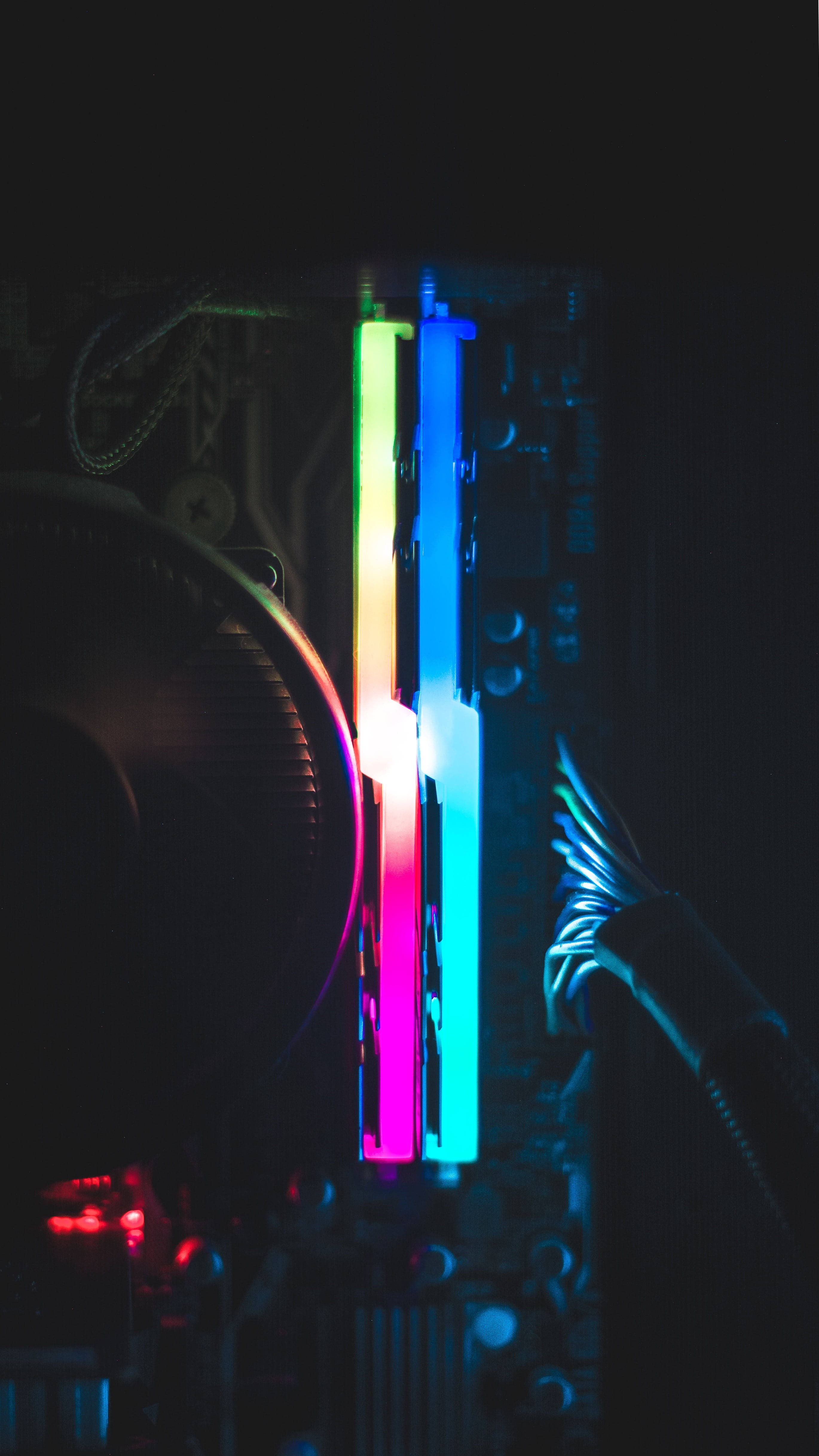 Dark Neon 桌布 壁紙 — 鮮豔的彩虹LED燈垂直發光在黑暗的電腦主機板上，帶有散熱風扇和陰影中的電線。