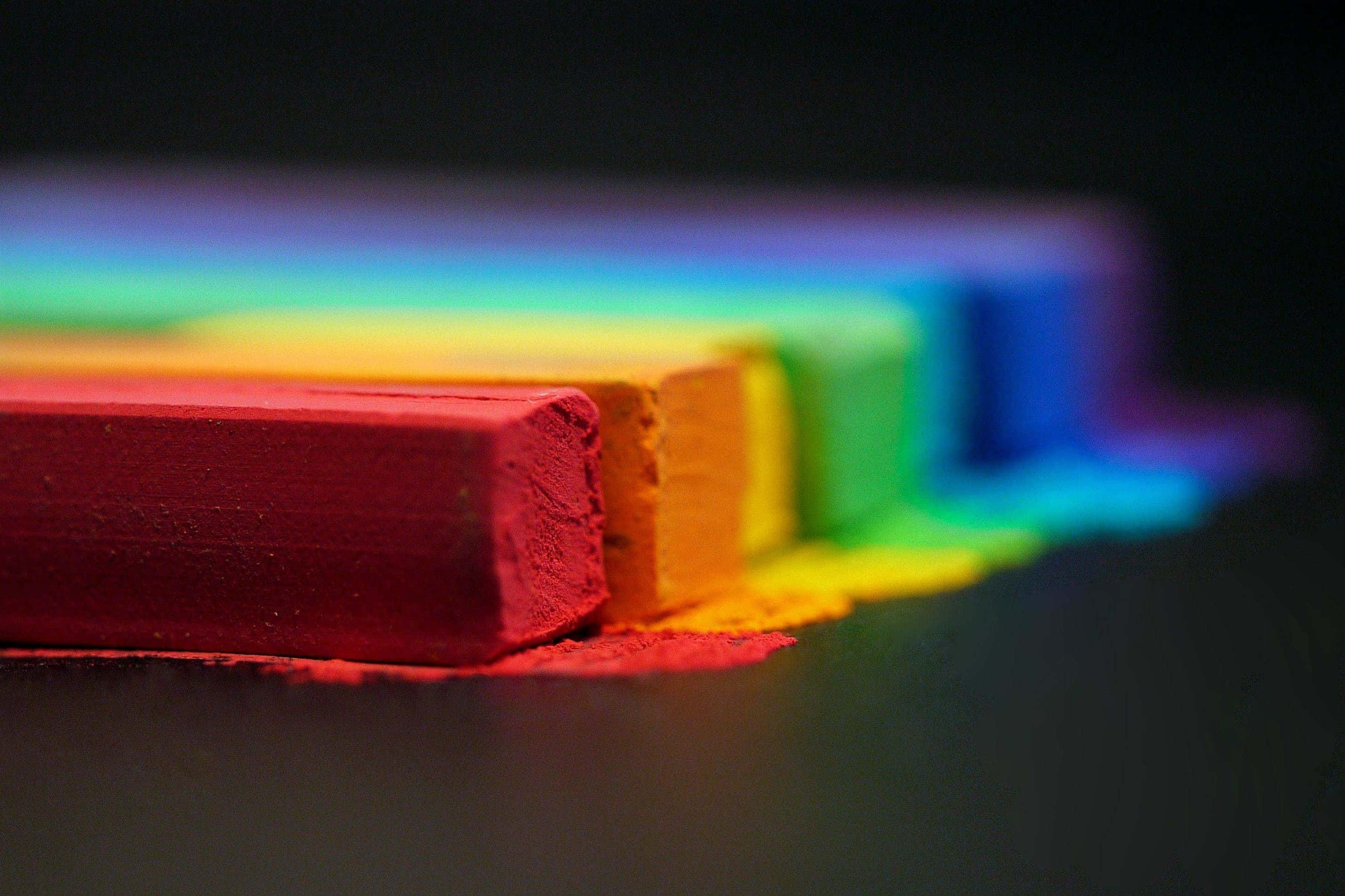 LGBT 桌布 壁紙 — 鮮豔的彩虹粉筆塊排成一列，背景柔和，灰塵散落在深色表面上。