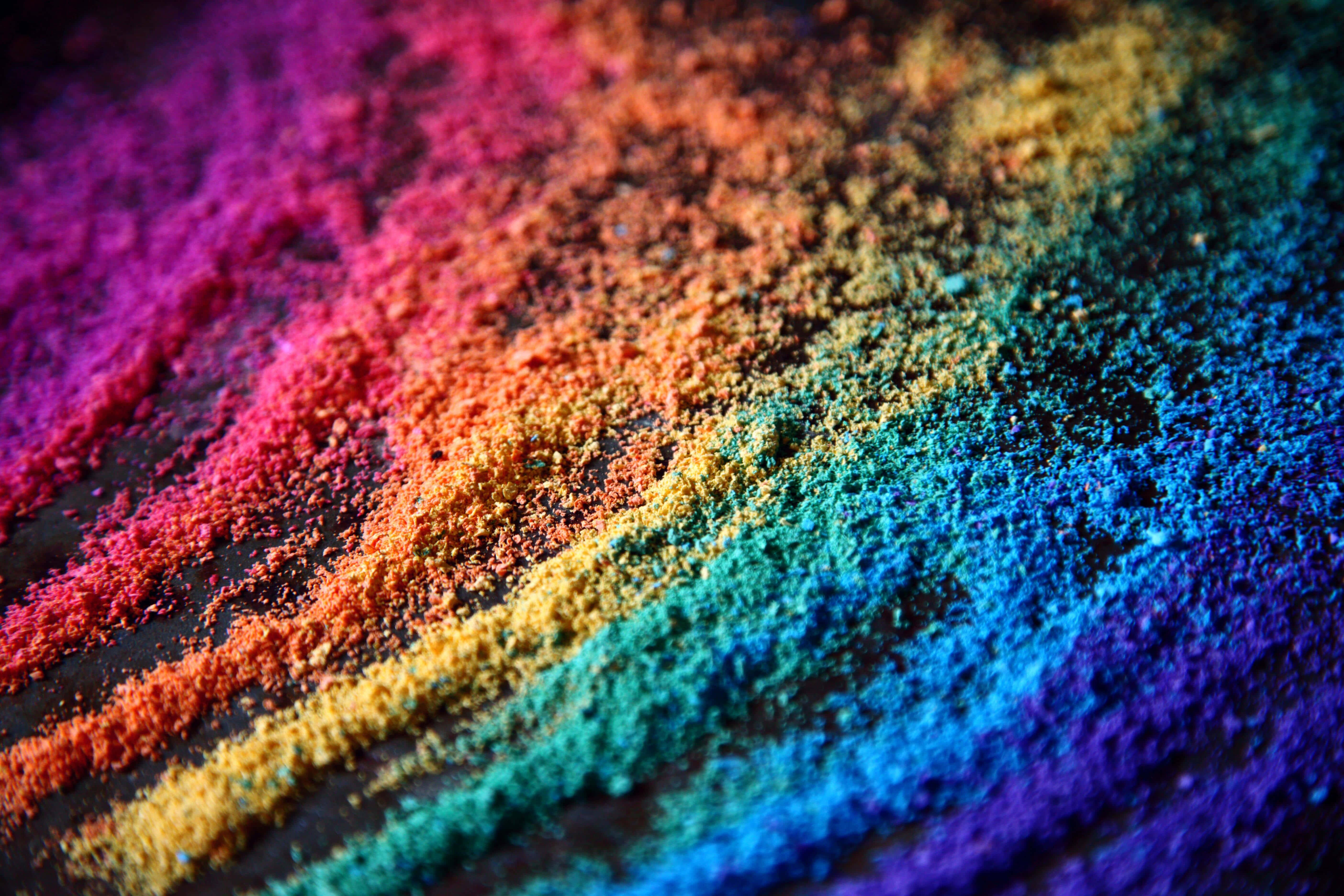 Holi 桌布 壁紙 — 鮮豔的彩虹色粉末塵埃痕跡在黑暗表面上對角線延伸，呈現生動的微距拍攝。