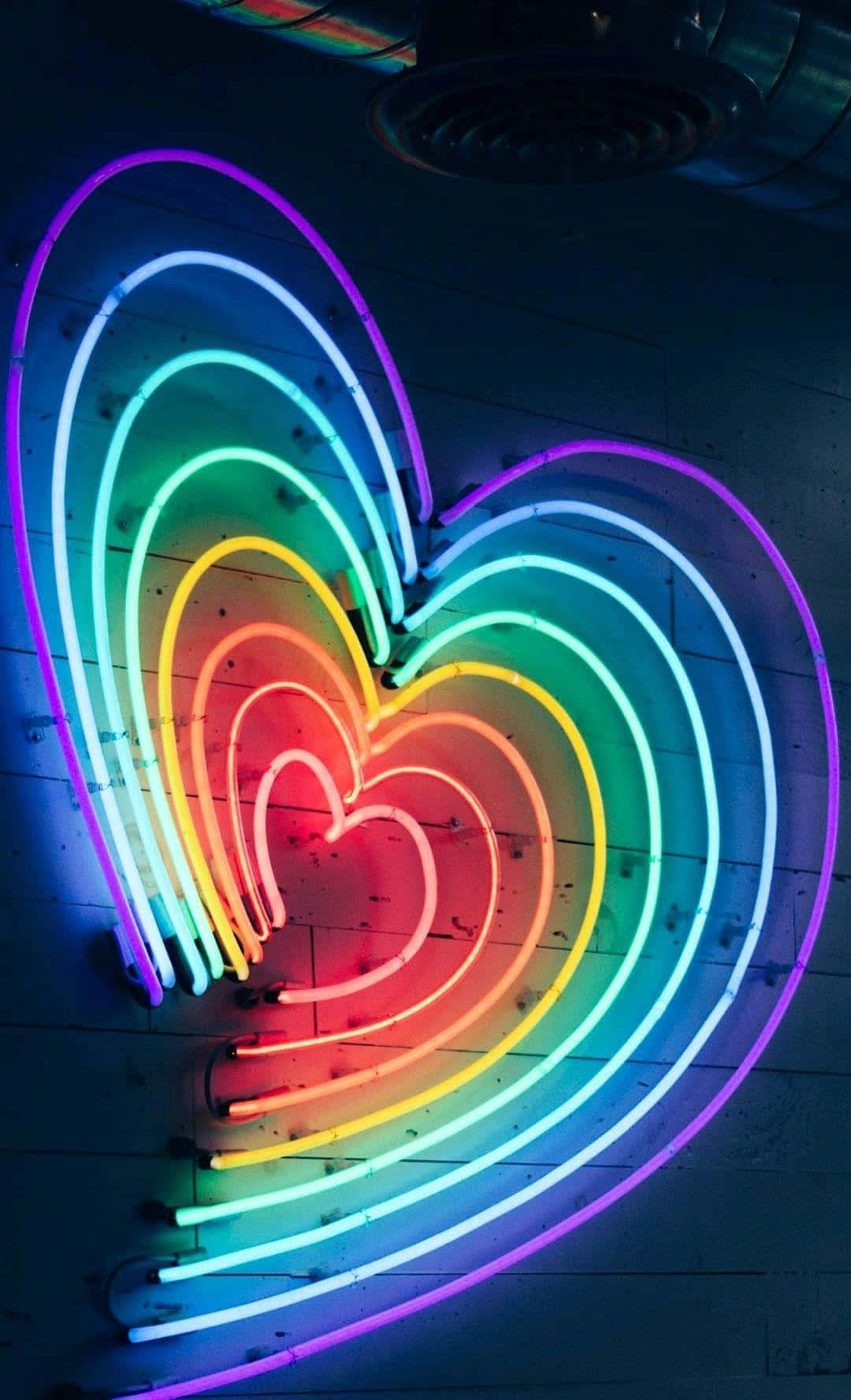 Rainbow Heart 桌布 壁紙 — 鮮豔的彩虹霓虹心形在深色木牆上以同心層次發光。