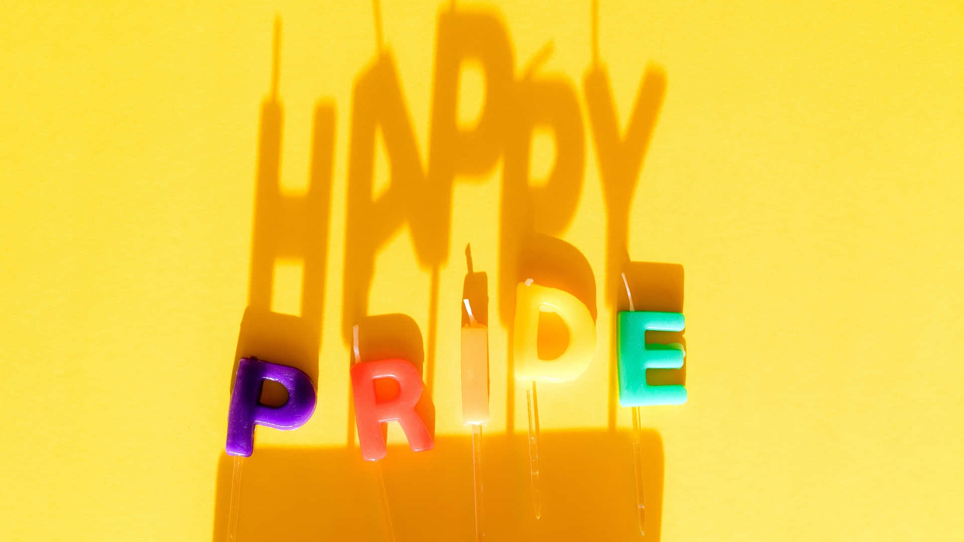 Pride Zoom 桌布 壁紙 — 鮮豔的彩虹驕傲字母在明亮的黃色背景上投射出大膽的陰影。