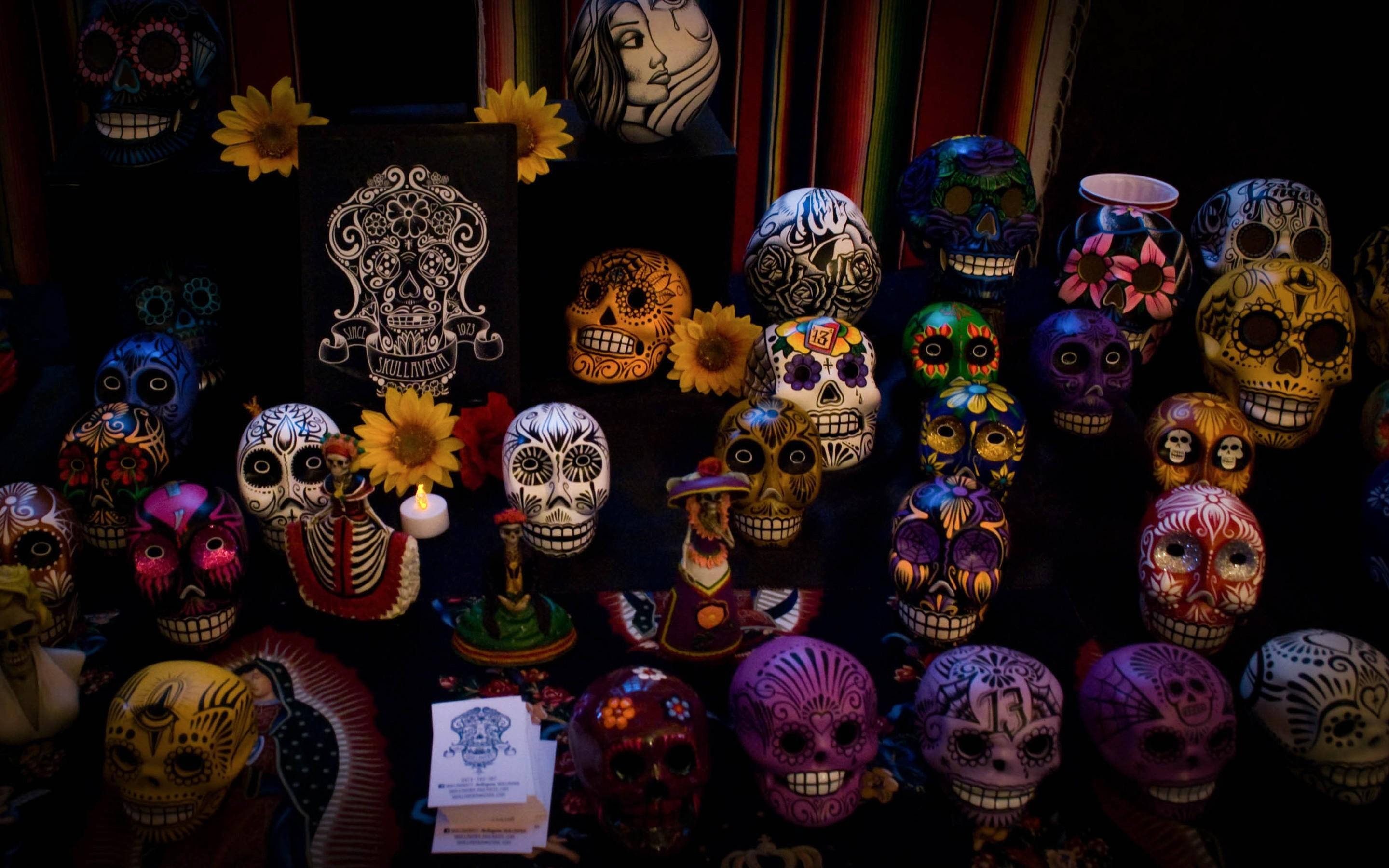 Dia De Los Muertos 桌布 壁紙 — 鮮豔的手繪糖骷髏在燭光下溫暖地發光，背景是深色，點綴著萬壽菊和傳統紡織品。