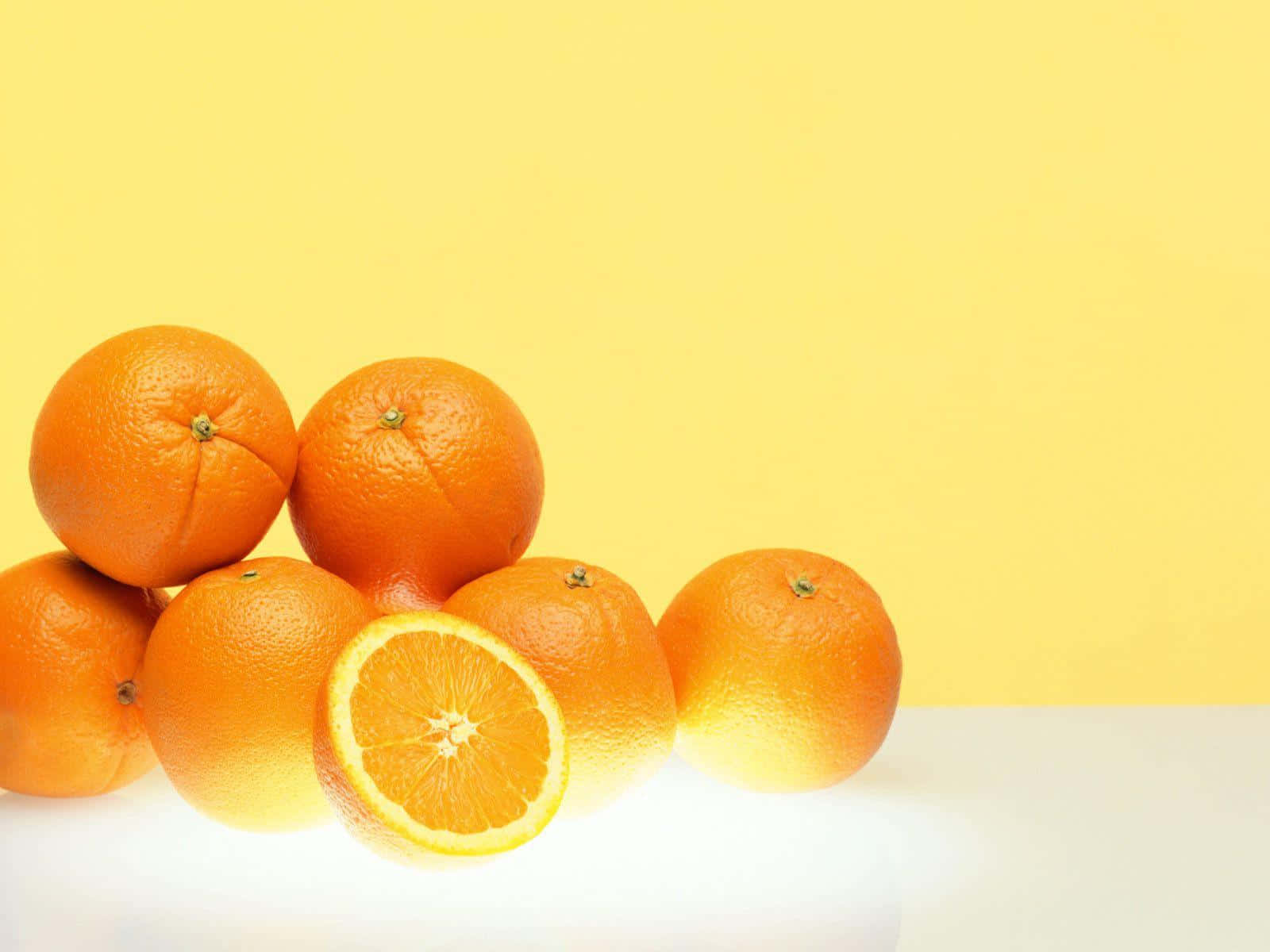 Orange Fruit 桌布 壁紙 — 鮮豔的柳橙堆放在明亮的黃色背景上，其中一個切開，露出多汁的果瓣。