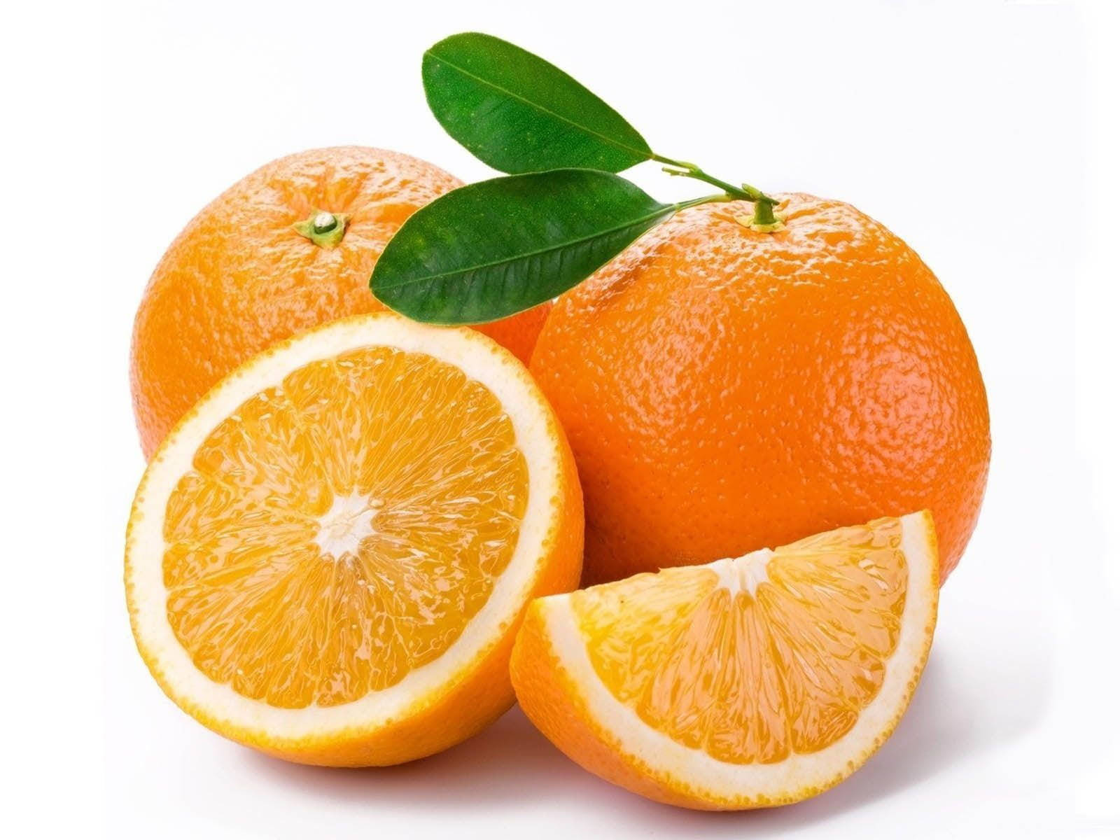 Fruits 桌布 壁紙 — 鮮豔的柳橙搭配綠葉，一片切開露出多汁的果瓣，襯以潔淨的白色背景。