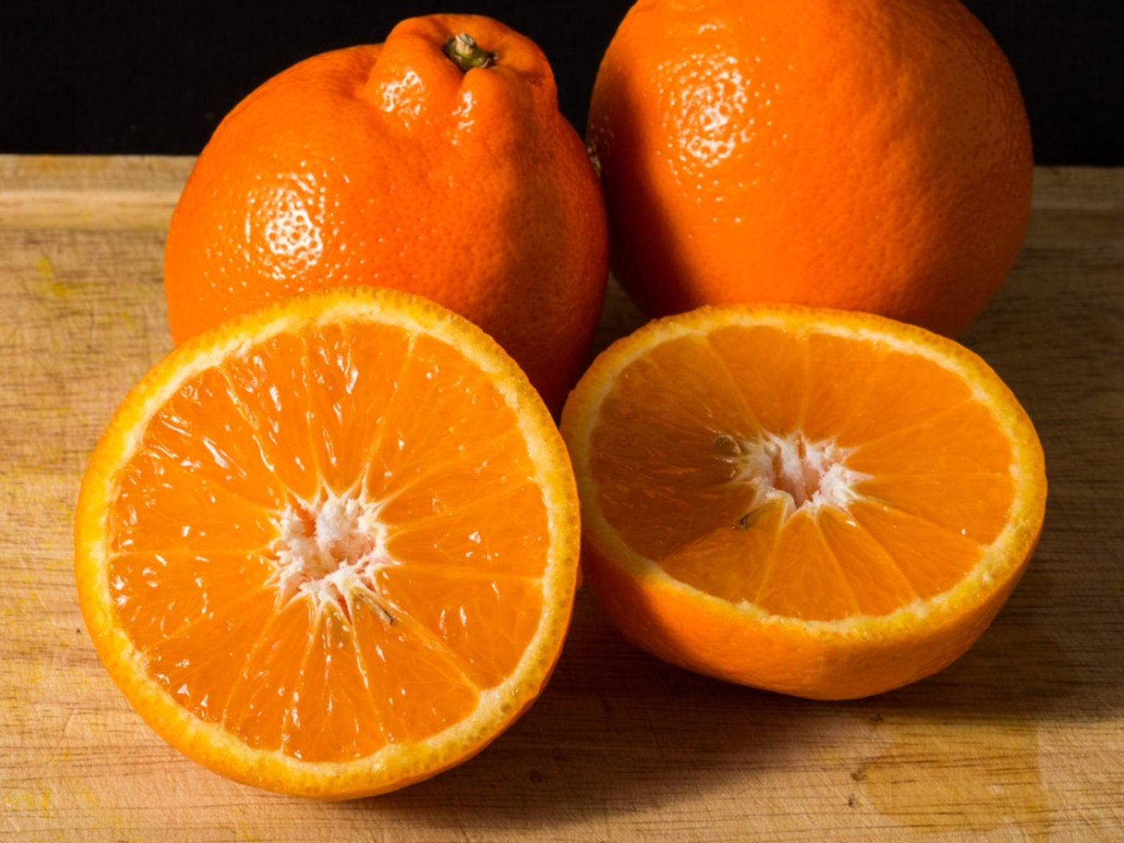 Fruits 桌布 壁紙 — 鮮豔的橙半邊和完整水果在溫暖燈光下在質樸木砧板上閃閃發光。
