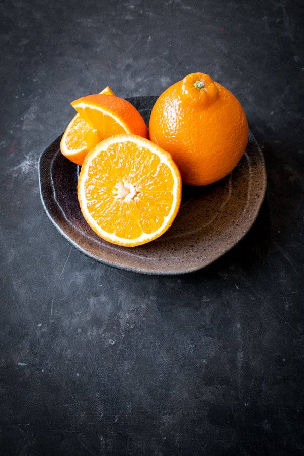 Fruits 桌布 壁紙 — 鮮豔的橙片和整個橙子放在一個質樸的陶瓷盤子上，背景是深色紋理。
