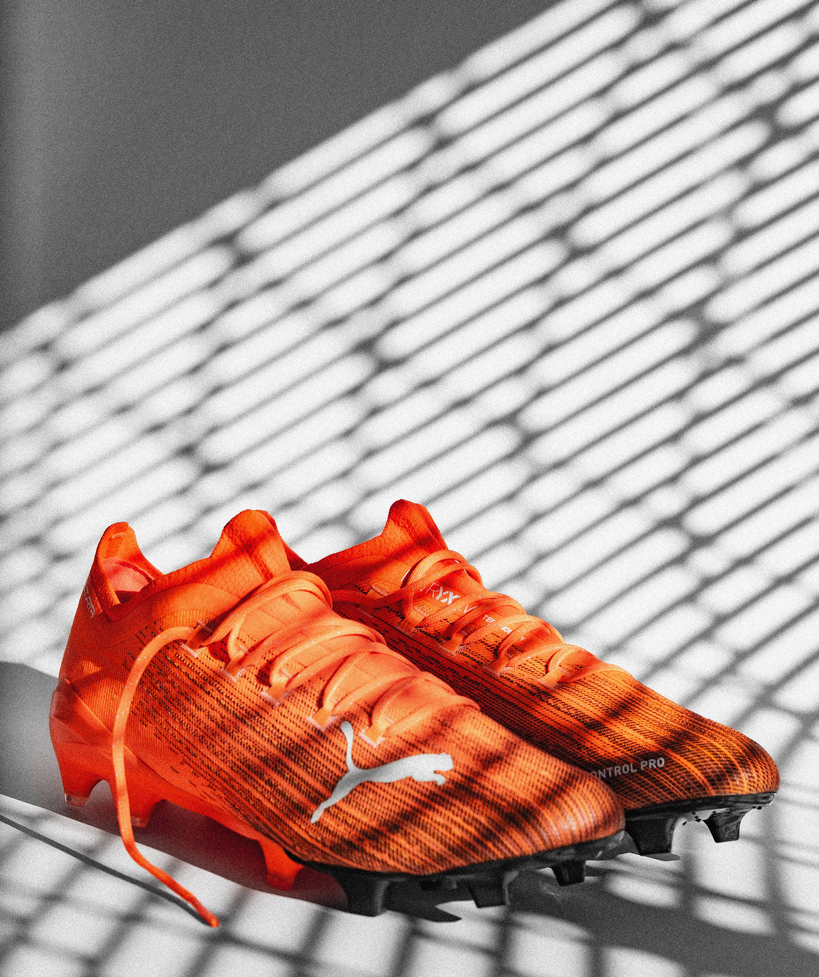 Puma 桌布 壁紙 — 鮮豔的橙色 Puma 足球鞋在單色表面上，置於銳利的幾何陰影下。