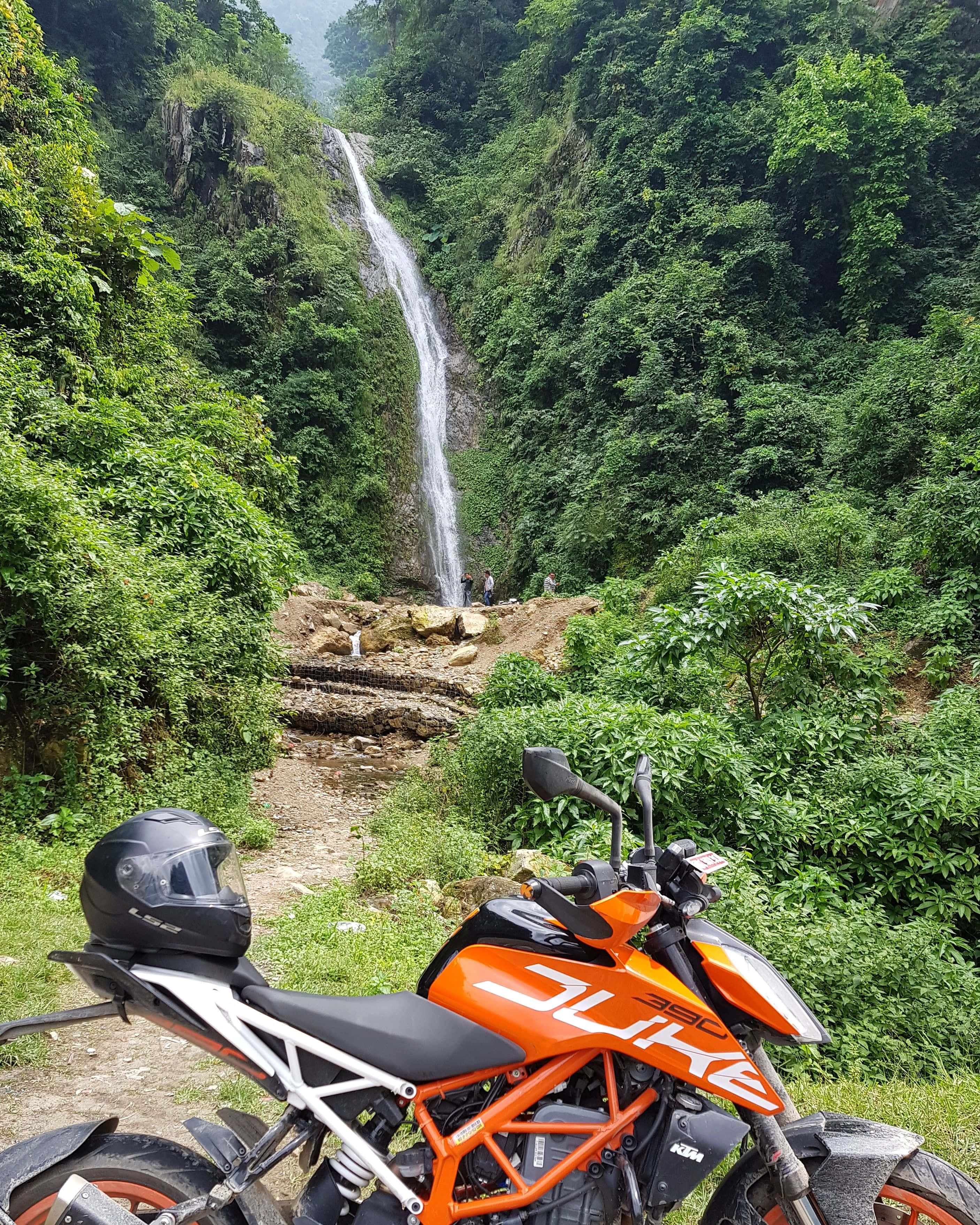 機車 桌布 壁紙 — 鮮豔的橙色KTM Duke摩托車停泊在霧氣瀰漫的叢林山谷中一個翠綠瀑布的底部。