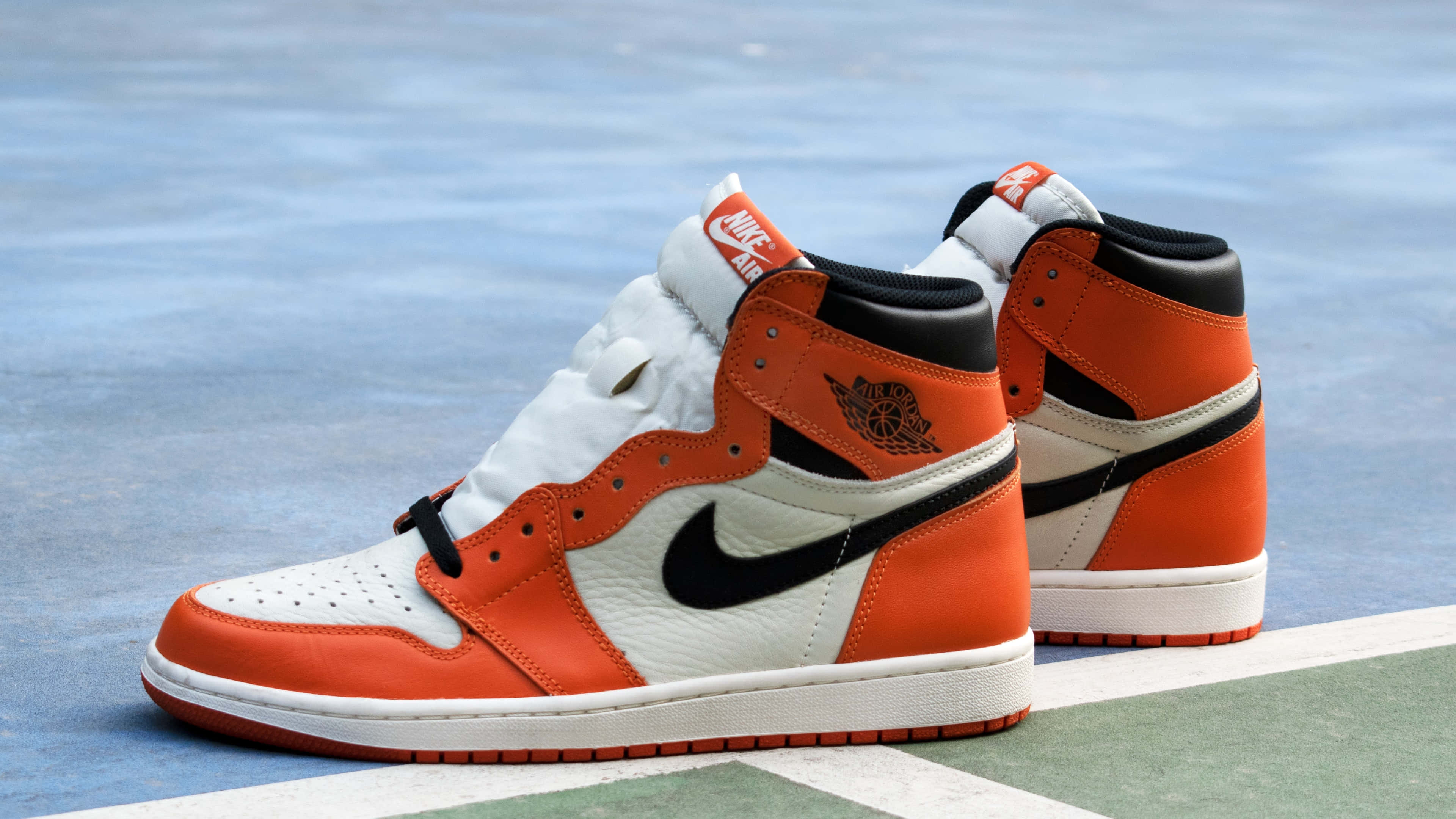 桌布 壁紙 — 鮮豔的橙色和白色 Air Jordan 1 運動鞋放在藍色和綠色的籃球場表面上。