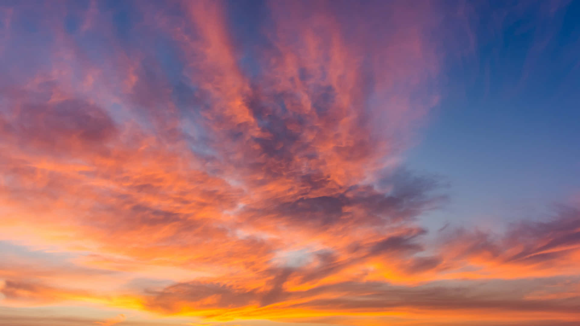 夕陽天空 桌布 壁紙 — 鮮豔的橙色和粉紅色雲彩劃過深藍色的暮色天空，形成戲劇性的日落場景。
