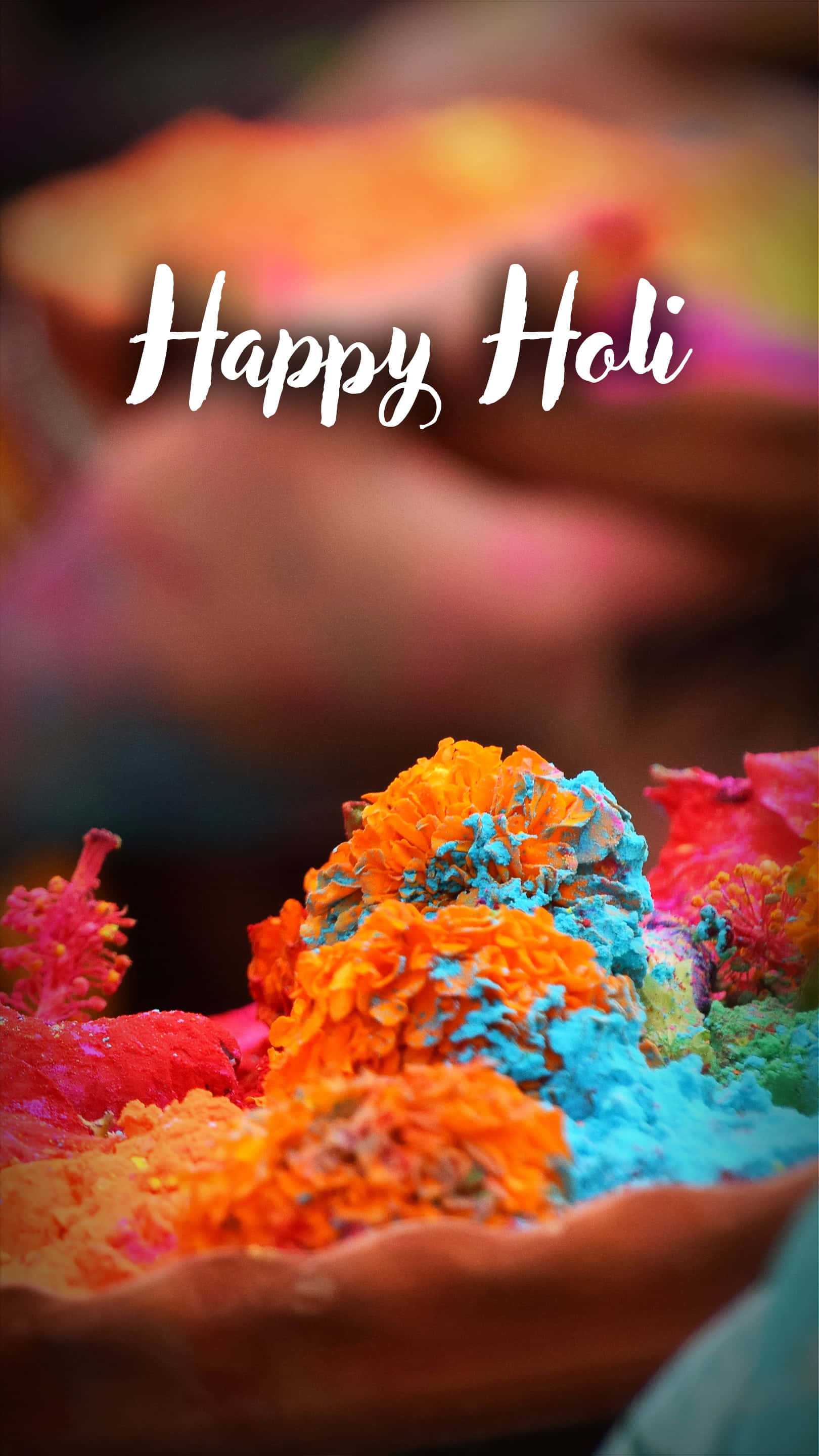 Holi 桌布 壁紙 — 鮮豔的橙色和藍色彩色粉末從一個粘土碗中溢出，背景是模糊的節日場景和慶祝文字。