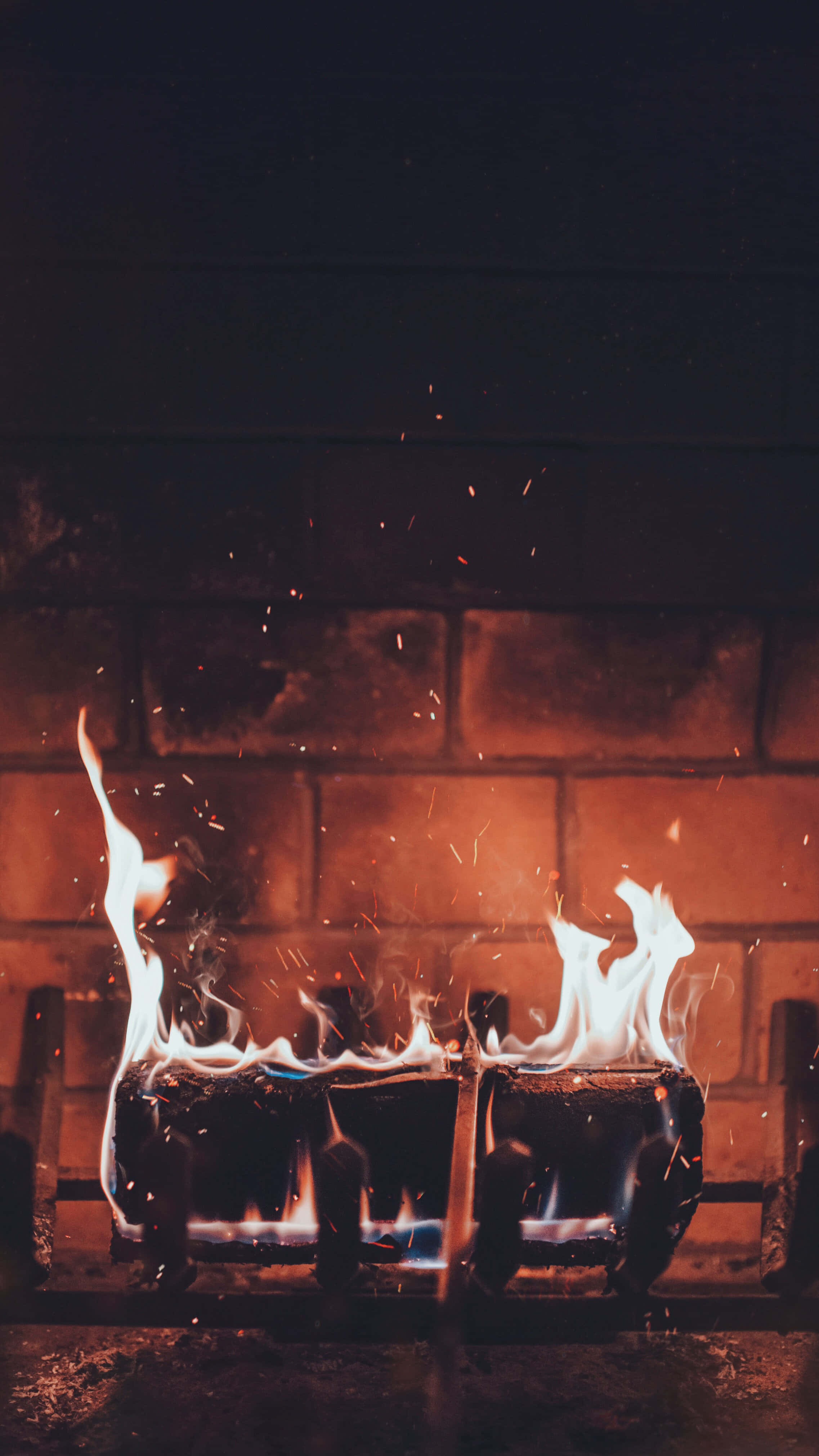 Autumn Fireplace 桌布 壁紙 — 鮮豔的橙色和藍色火焰在深色磚牆前從瓦斯爐爐頭中充滿活力地舞動。