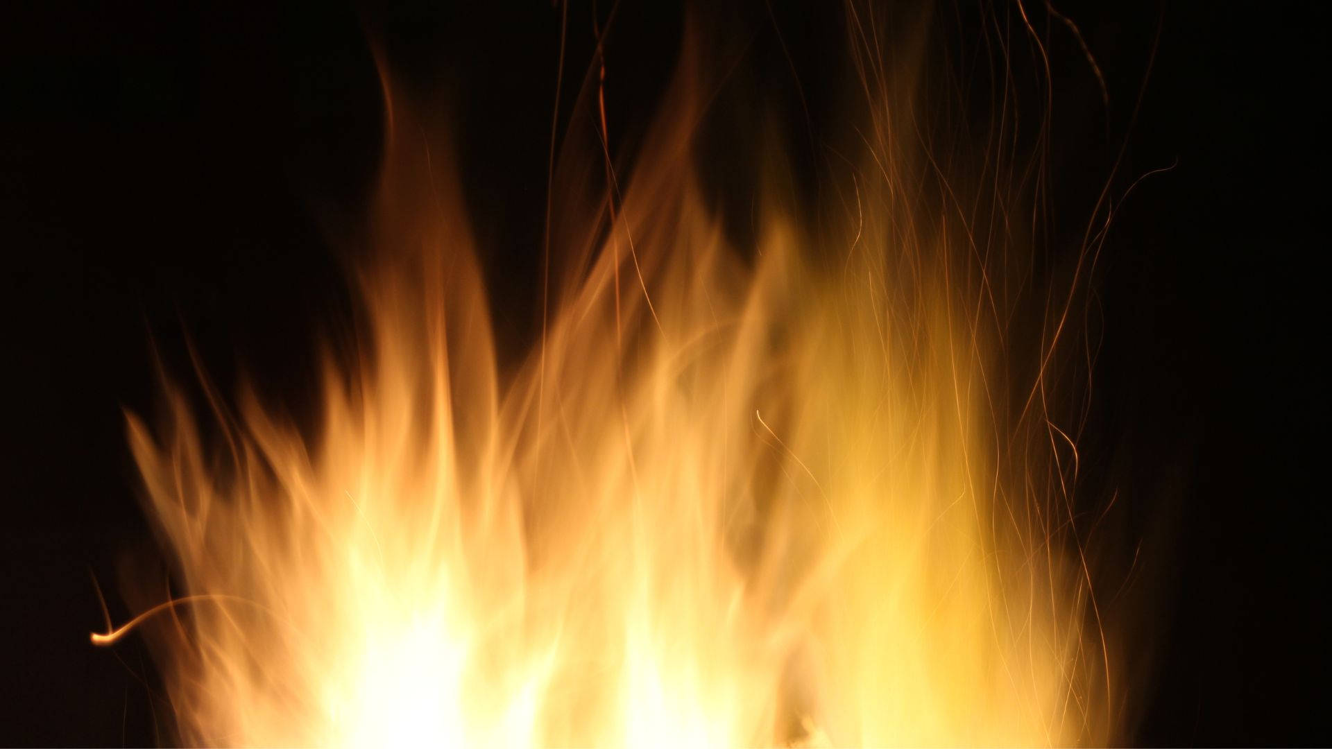 火焰動畫 桌布 壁紙 — 鮮豔的橙色和黃色火焰在漆黑的背景下動態上升，發光的餘燼向上飄散。
