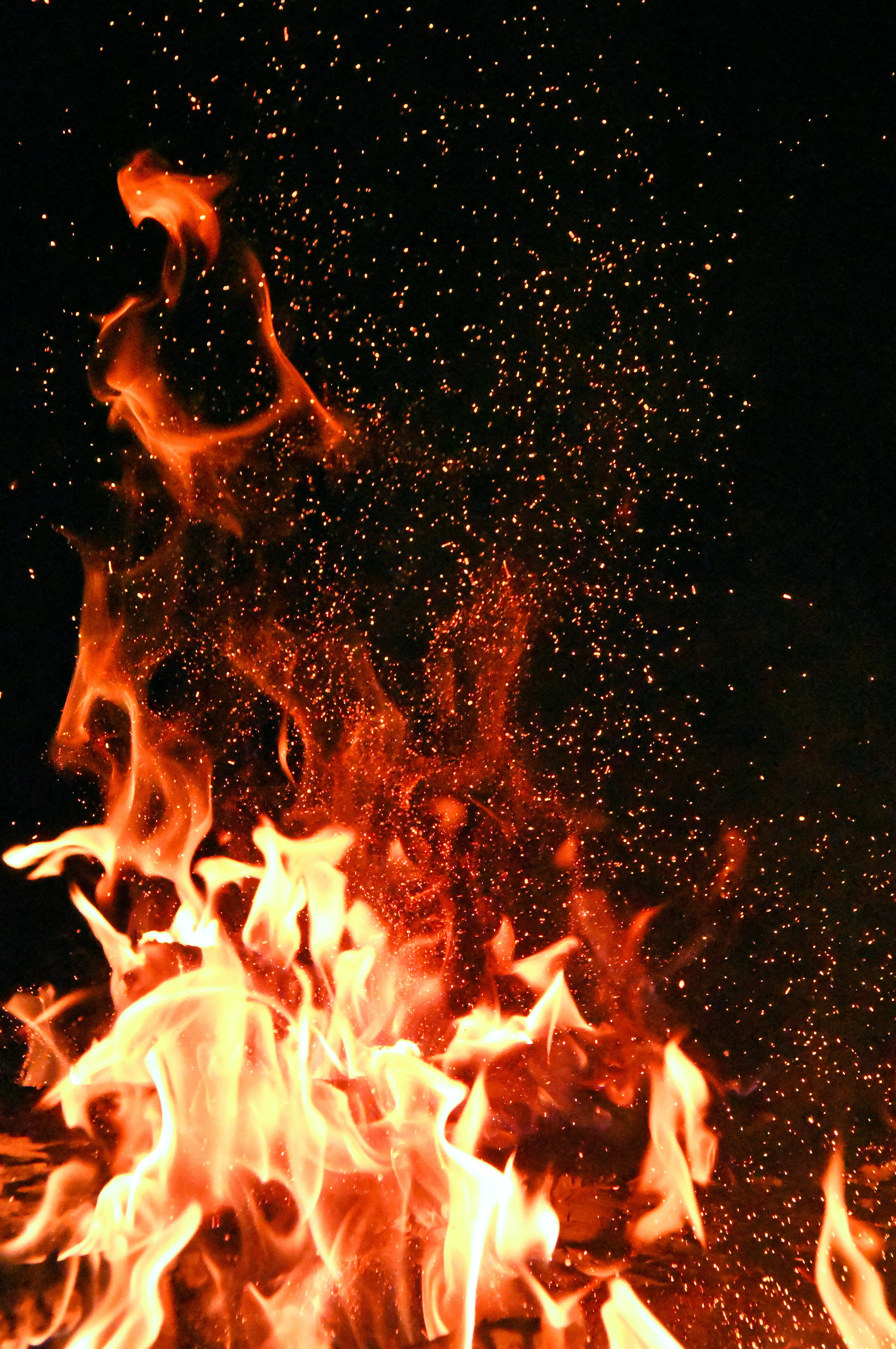 暗紅色 桌布 壁紙 — 鮮豔的橙色和黃色火焰在漆黑的背景上猛烈向上竄升，空中漂浮著發光的餘燼。